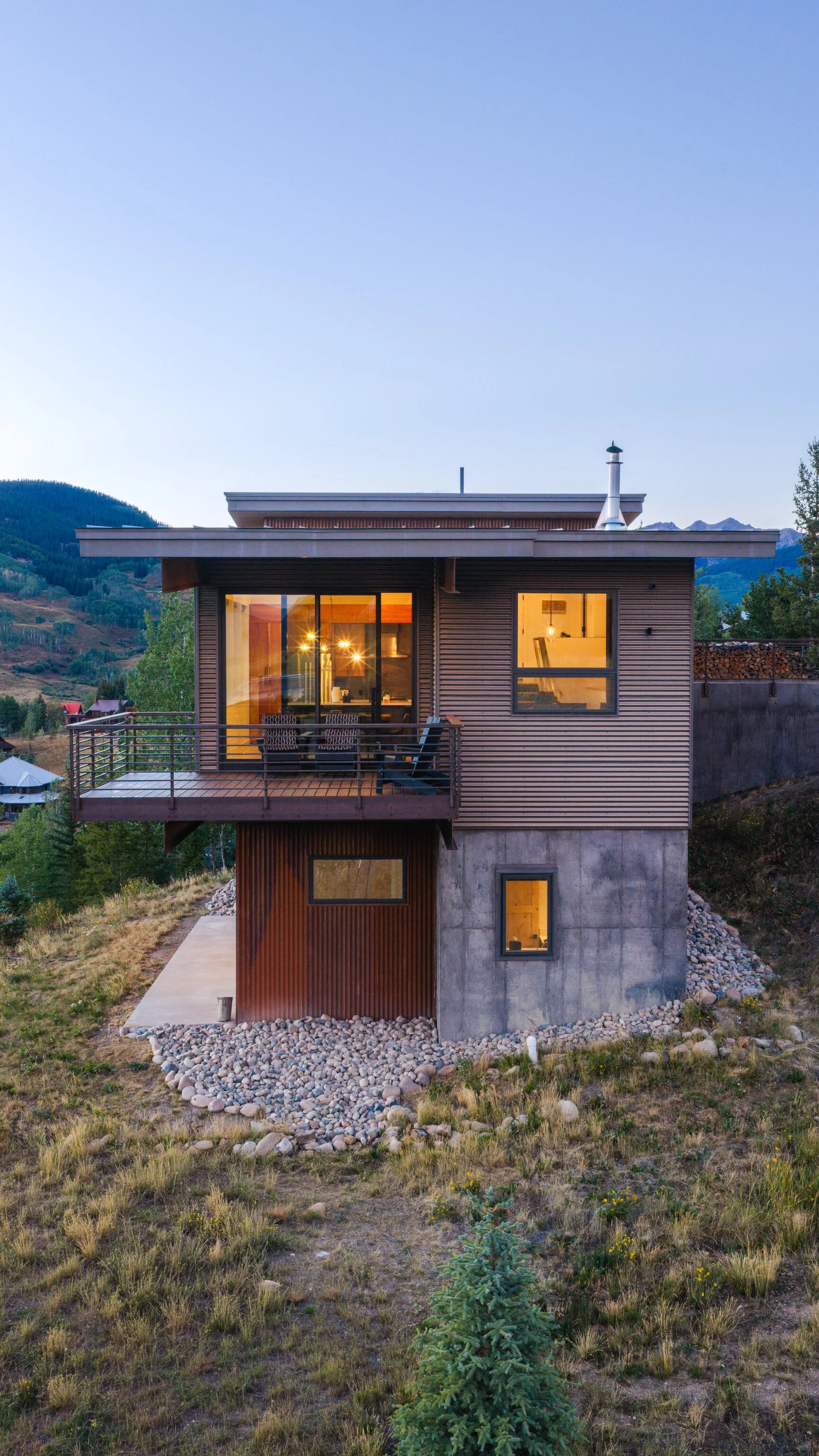 Modern high-performance home glowing from within at dusk, showing illuminated interior through large glazing, Gunnison Valley, Colorado