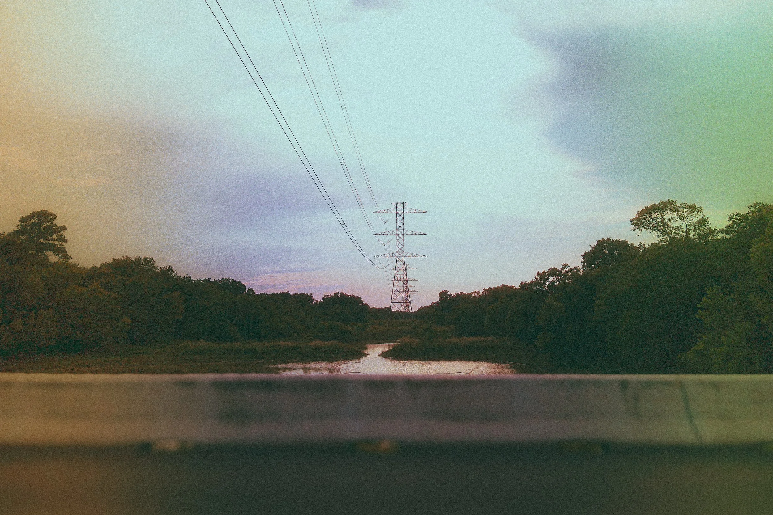 A landscape scene viewed from a car window showing a winding river, trees, and power lines against a dusk sky.