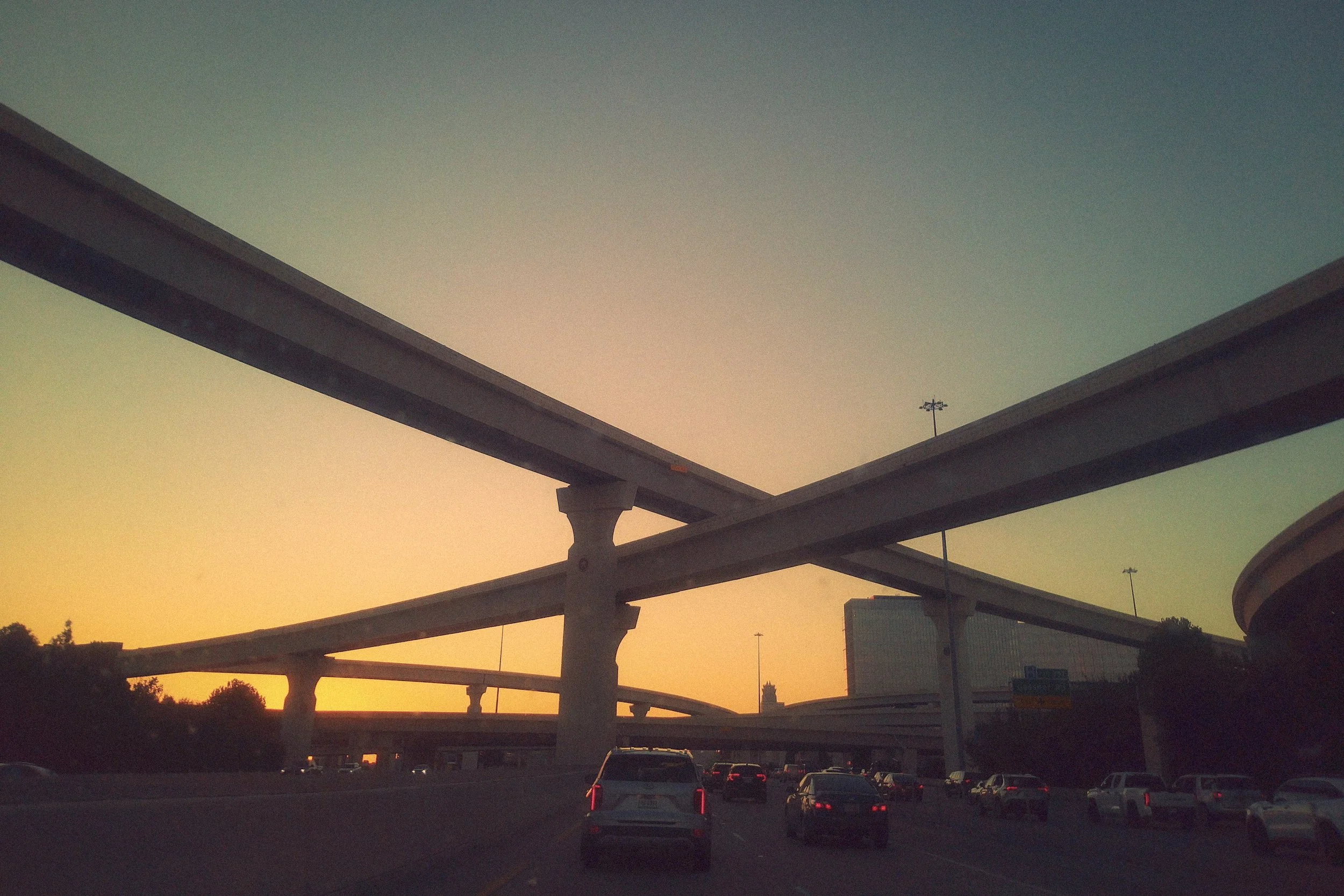 Highway overpass during sunrise with vehicles underneath and trees in the background.