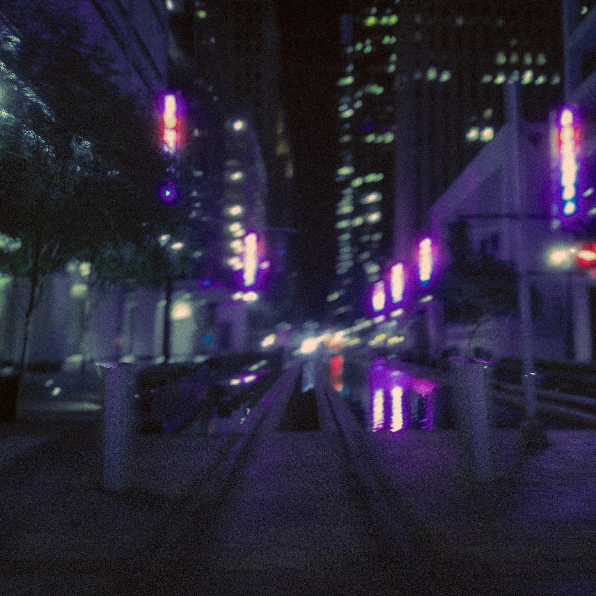 Blurred cityscape at night with colorful lights reflecting on water, possibly a river or a canal.