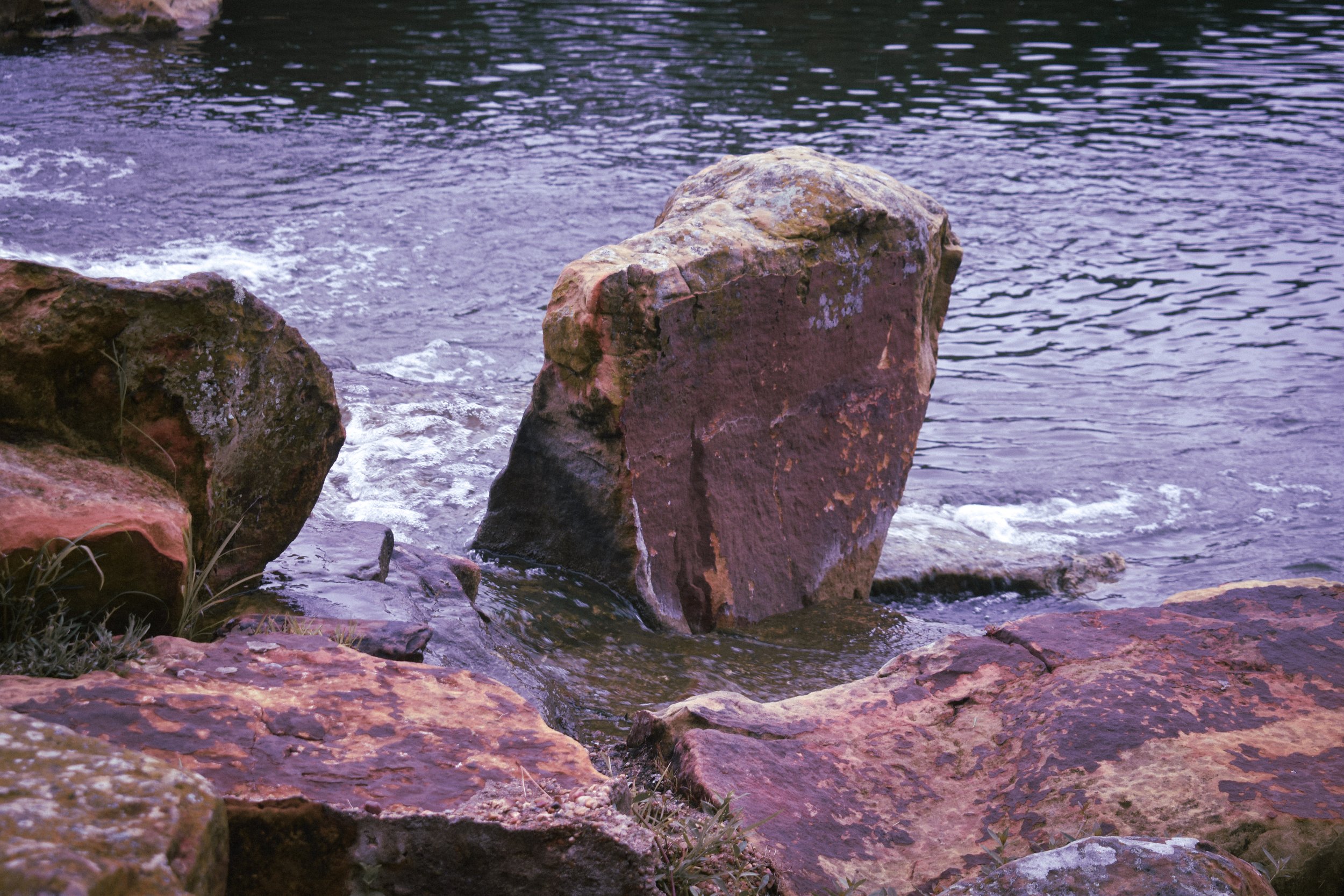 Large rocks near the edge of a body of water with small waves and ripples in a small lake, under a clear sky.