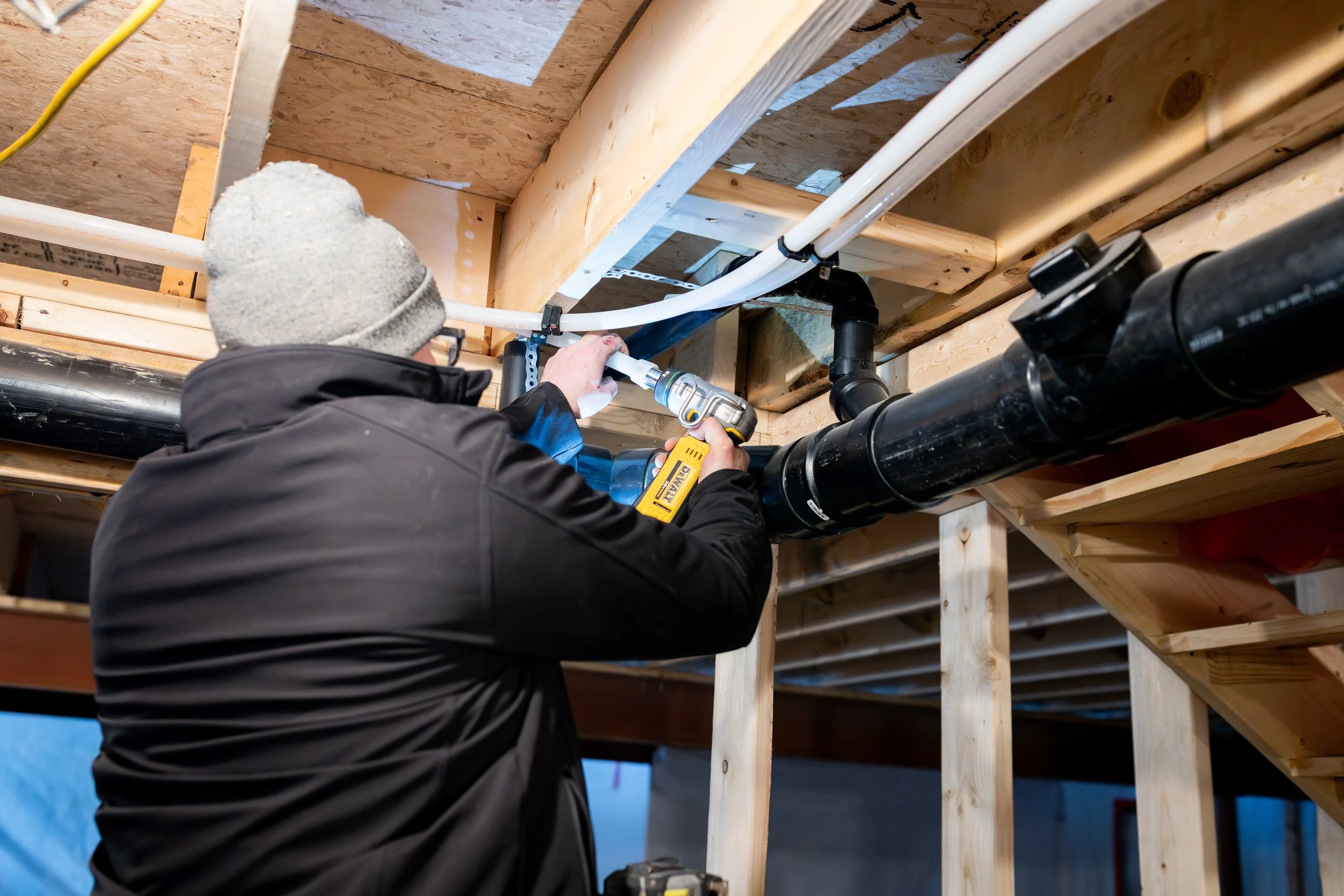 A construction worker installing plumbing pipes in a wooden framework of a building.