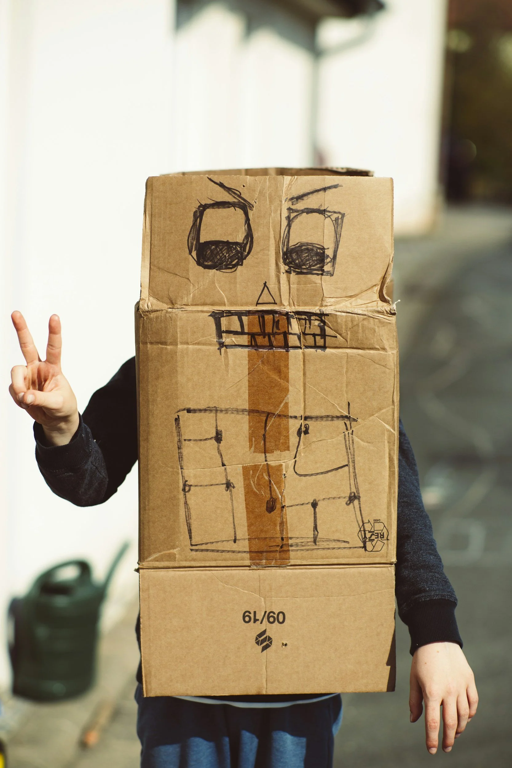 Child wearing a homemade cardboard robot Halloween costume with a hand-drawn face and details.