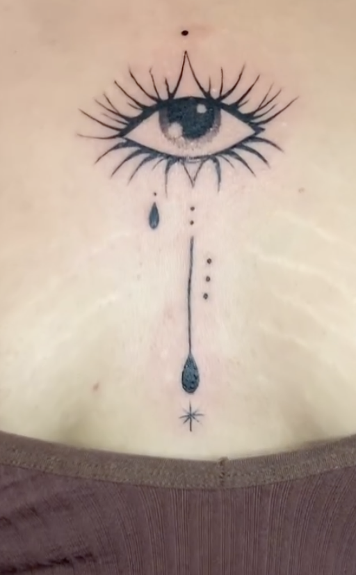 Ornamental eye tattoo with a dotted line down the sternum