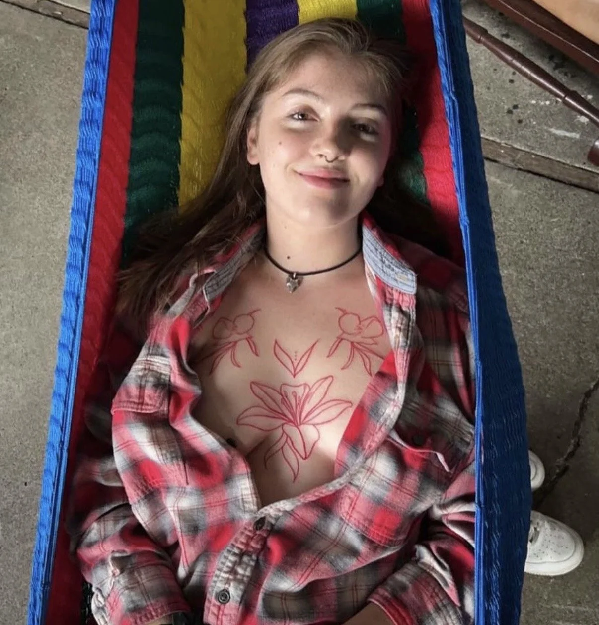 Client smiling in a hammock, showing a red floral chest tattoo