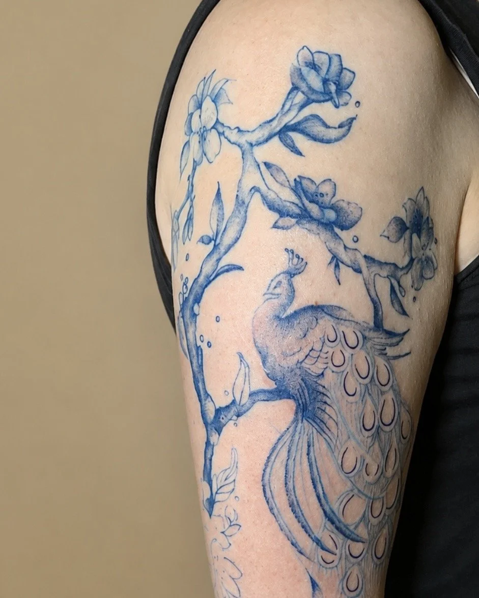 Blue-ink floral and bird tattoo on the upper arm