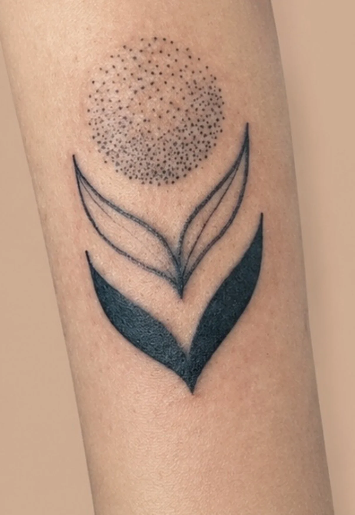 Stippled sun over a two-leaf design tattoo on the forearm