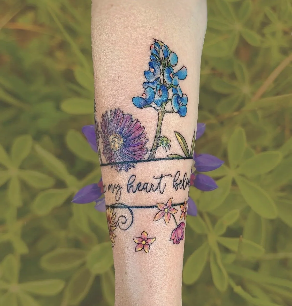 Wildflower band tattoo with script lettering around the forearm