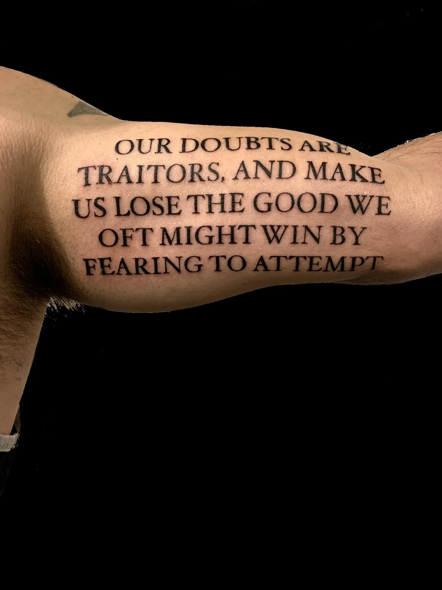 Script tattoo on the upper arm reading “Our doubts are traitors, and make us lose the good we oft might win by fearing to attempt”