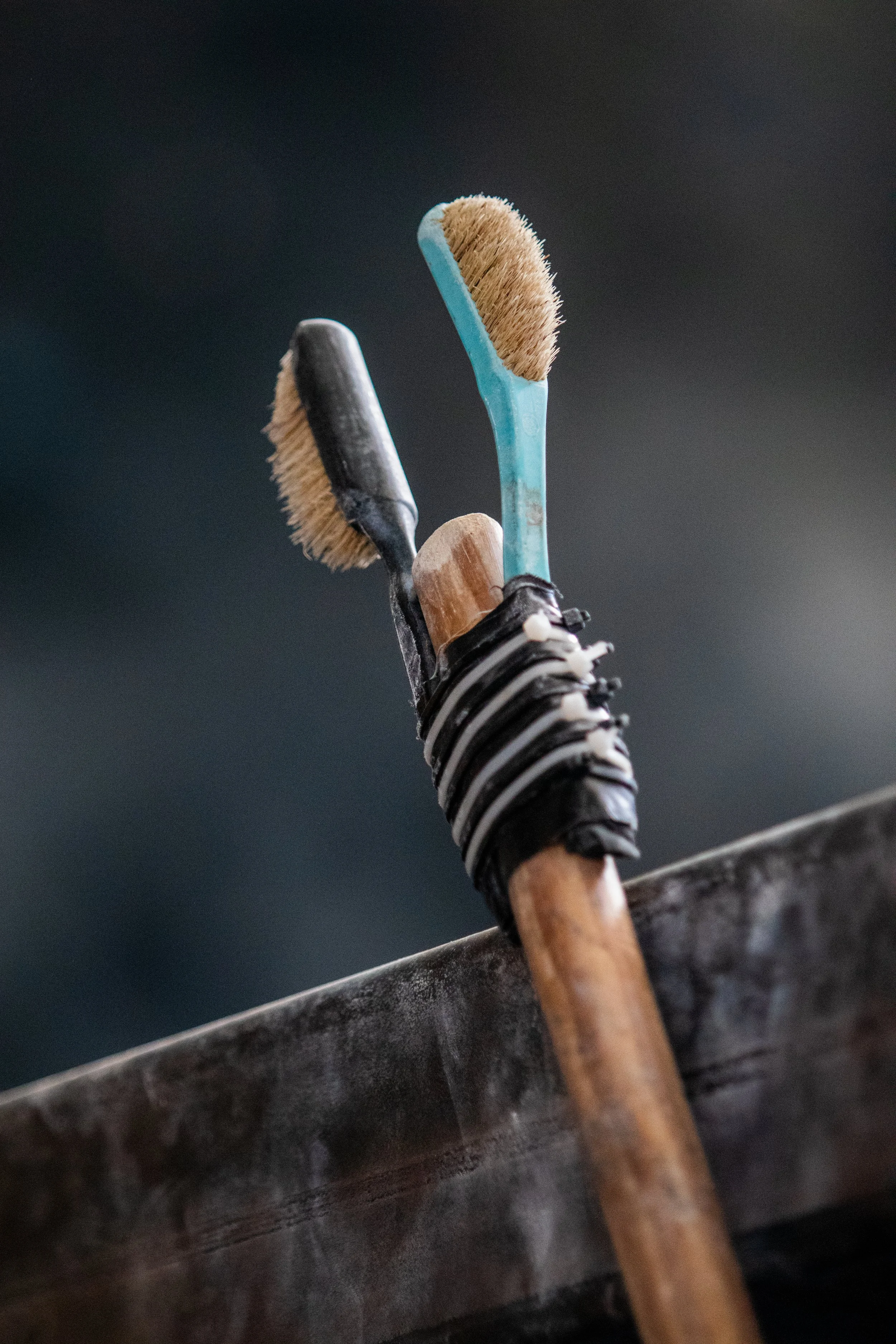Two wire brushes and a wooden-handled tool are placed in a container, with a dark, blurred background.