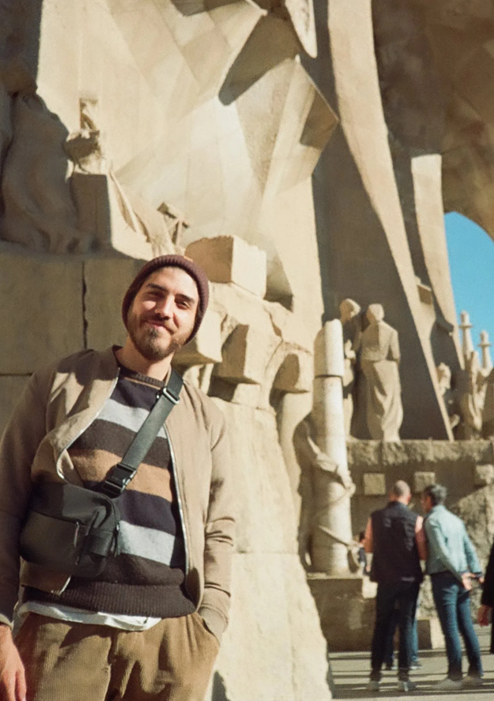 A man standing near the ancient stone sculptures of the Parthenon in Athens, Greece, with other tourists in the background.