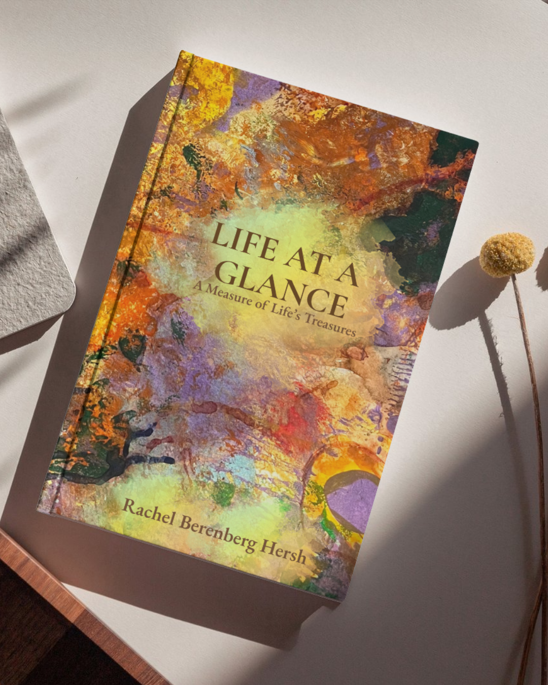 The cover of a book titled 'Life at a Glance: A Measure of Life's Treasures' by Rachel Berenberg Hersh. The cover features an abstract, colorful background with a mix of orange, yellow, purple, and green hues, resembling a watercolor painting.