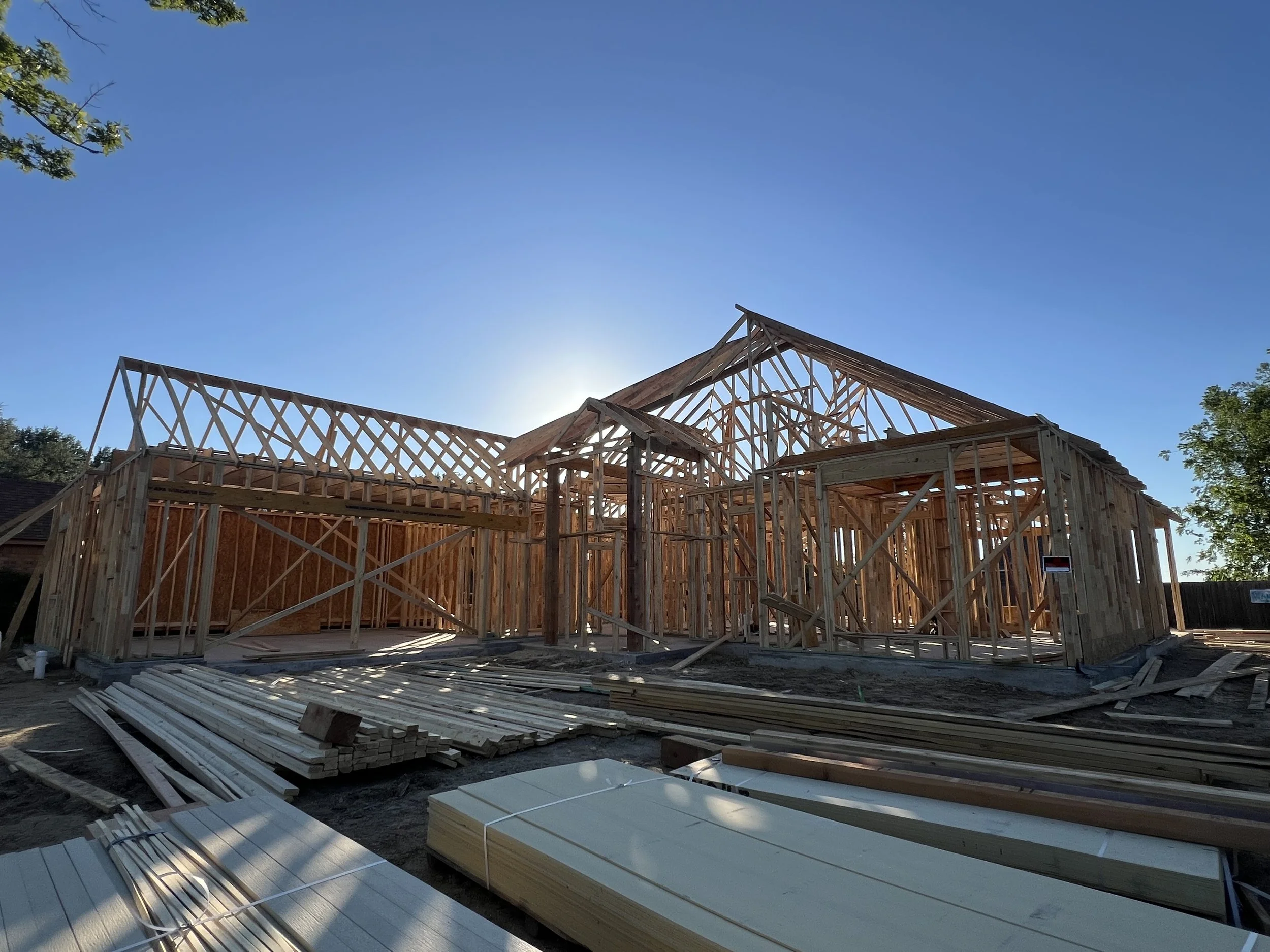 Wooden framing for a house under construction with clear blue sky and trees in the background.