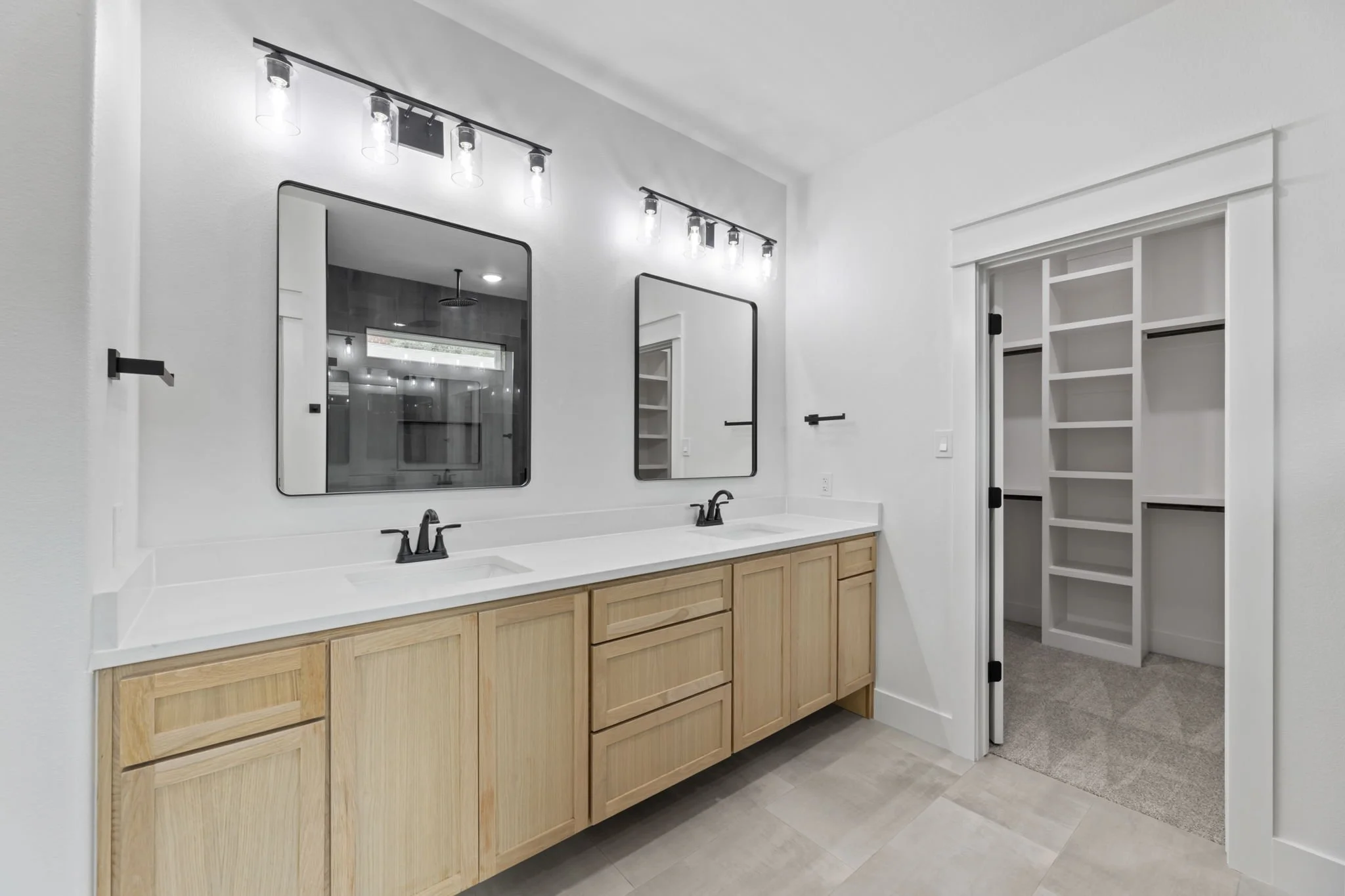 Modern bathroom with double vanity, black fixtures, two mirrors, and a doorway leading to a closet or storage space.