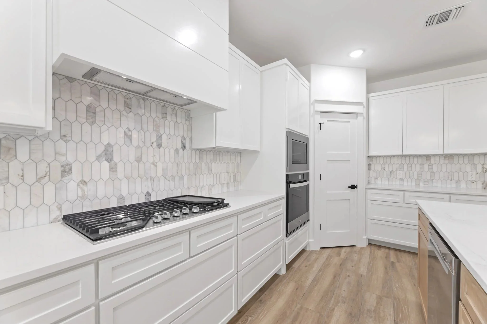 Modern white kitchen with tiled backsplash, gas stove, built-in oven, and white cabinetry.