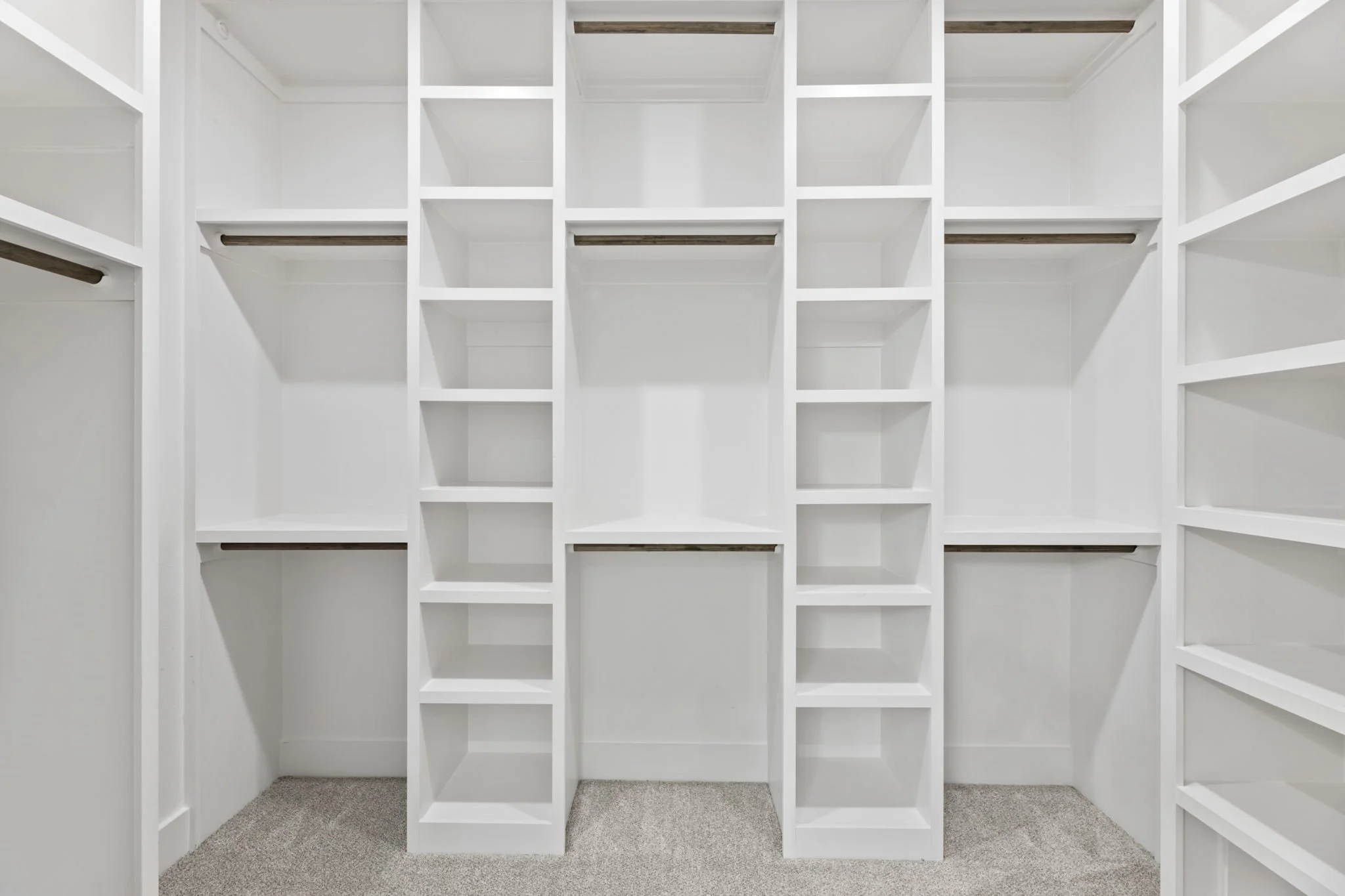 Empty white custom-built closet with multiple open shelves and hanging rods, carpeted floor.