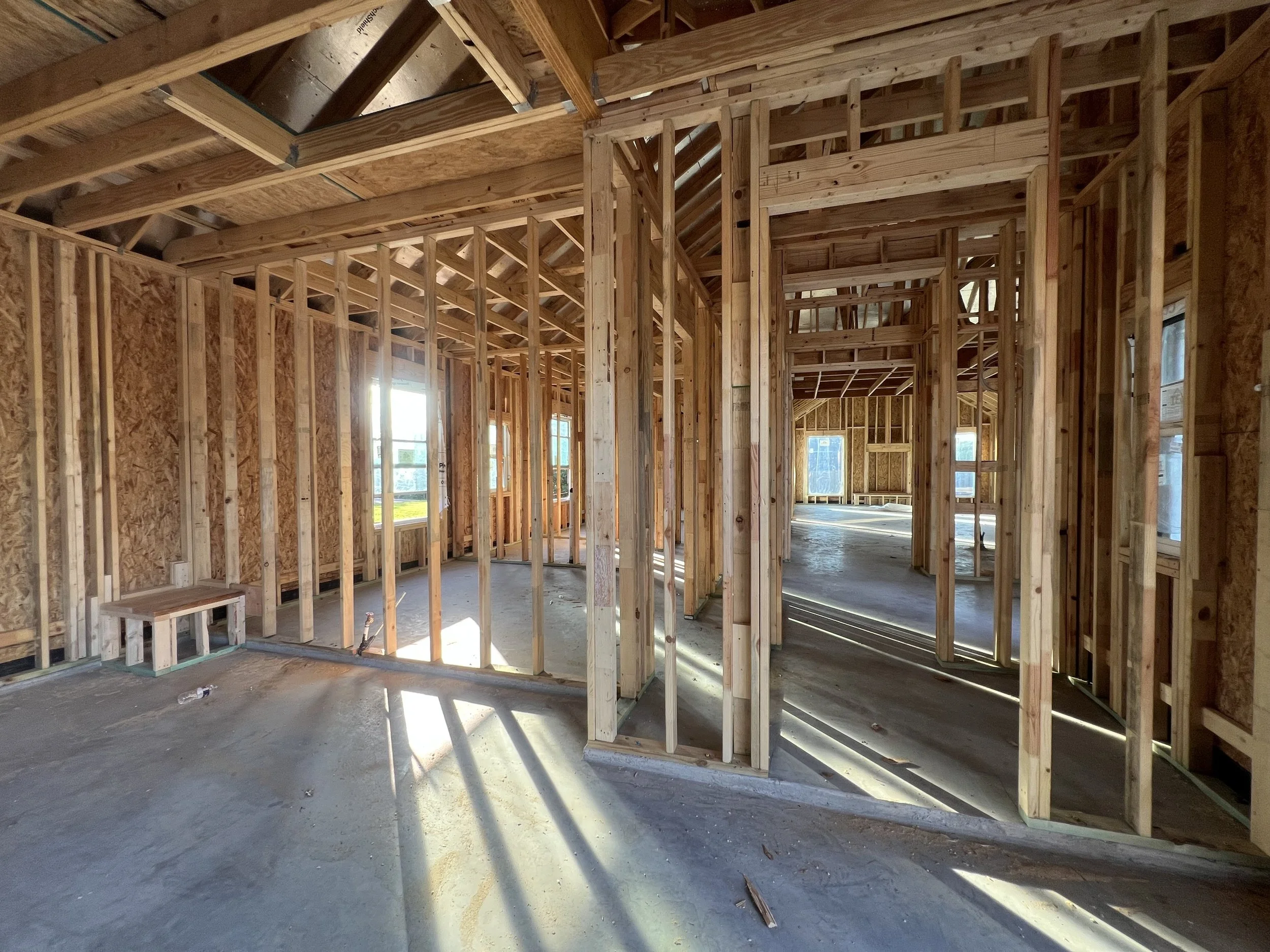 Interior of a house under construction with exposed wooden framing and some windows, showing the unfinished structure.
