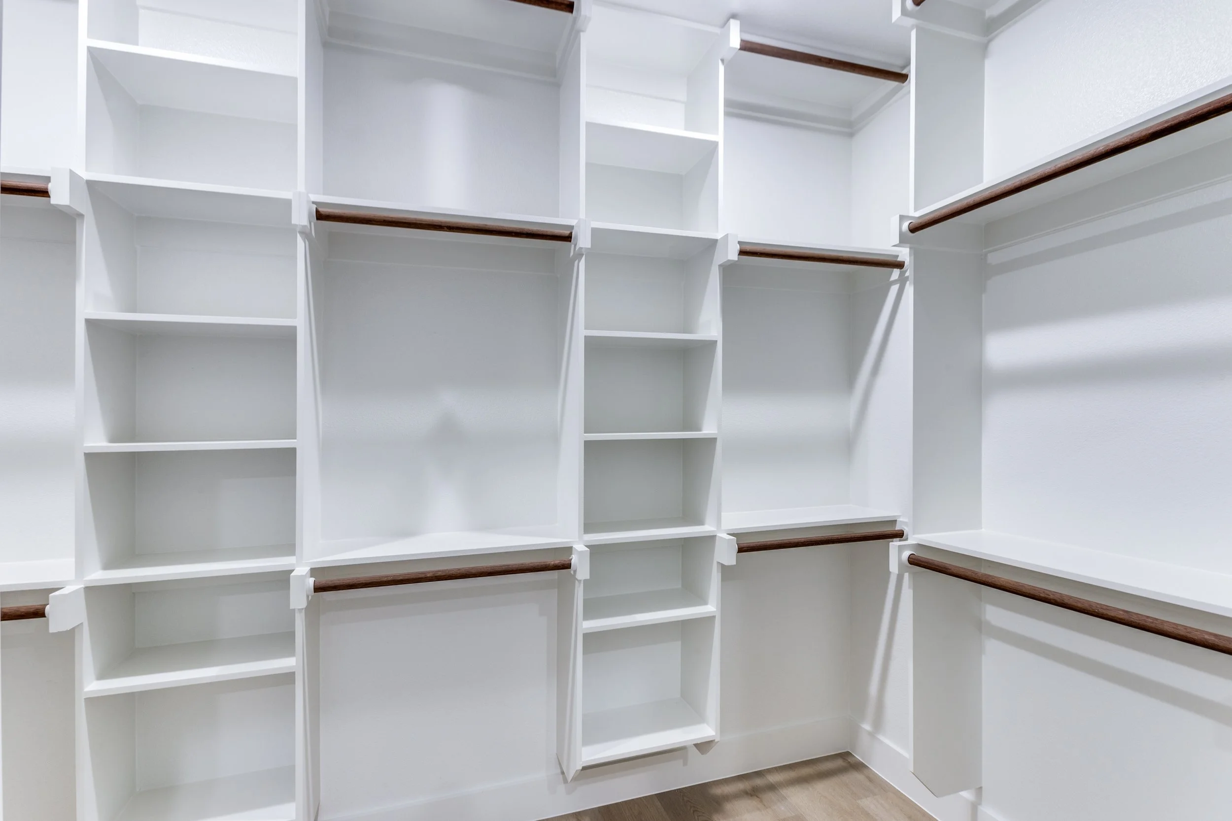 Empty walk-in closet with white shelves and brown hanging rods.