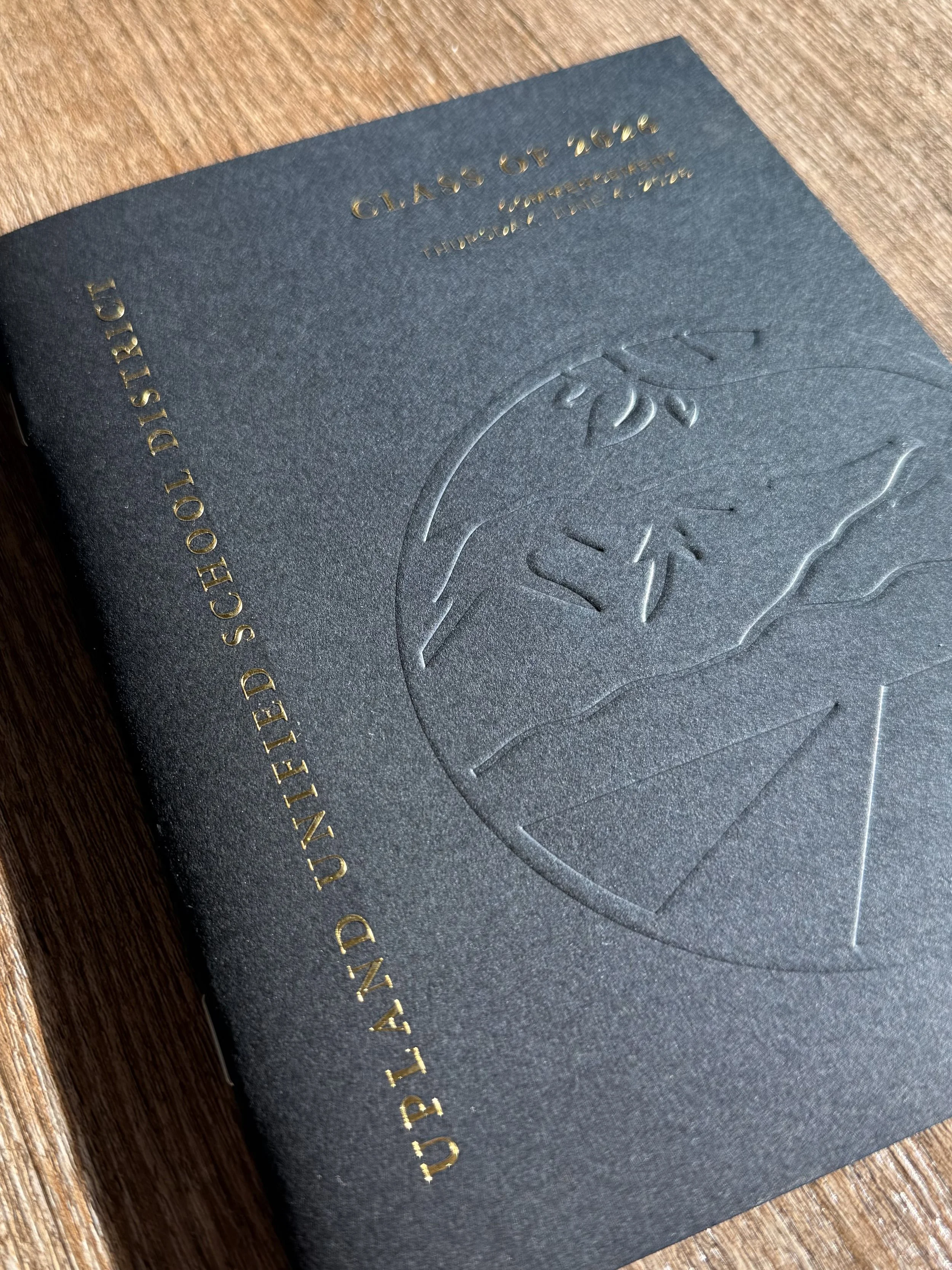 A black textured paper cover with embossed flowers and gold lettering on a wooden surface.
