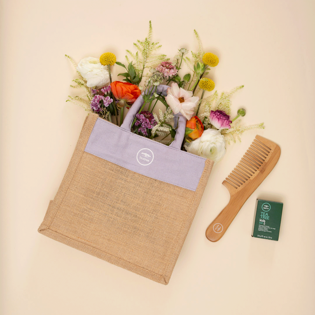 A tote bag filled with colorful flowers, a wooden comb, and a box of tea on a beige background.