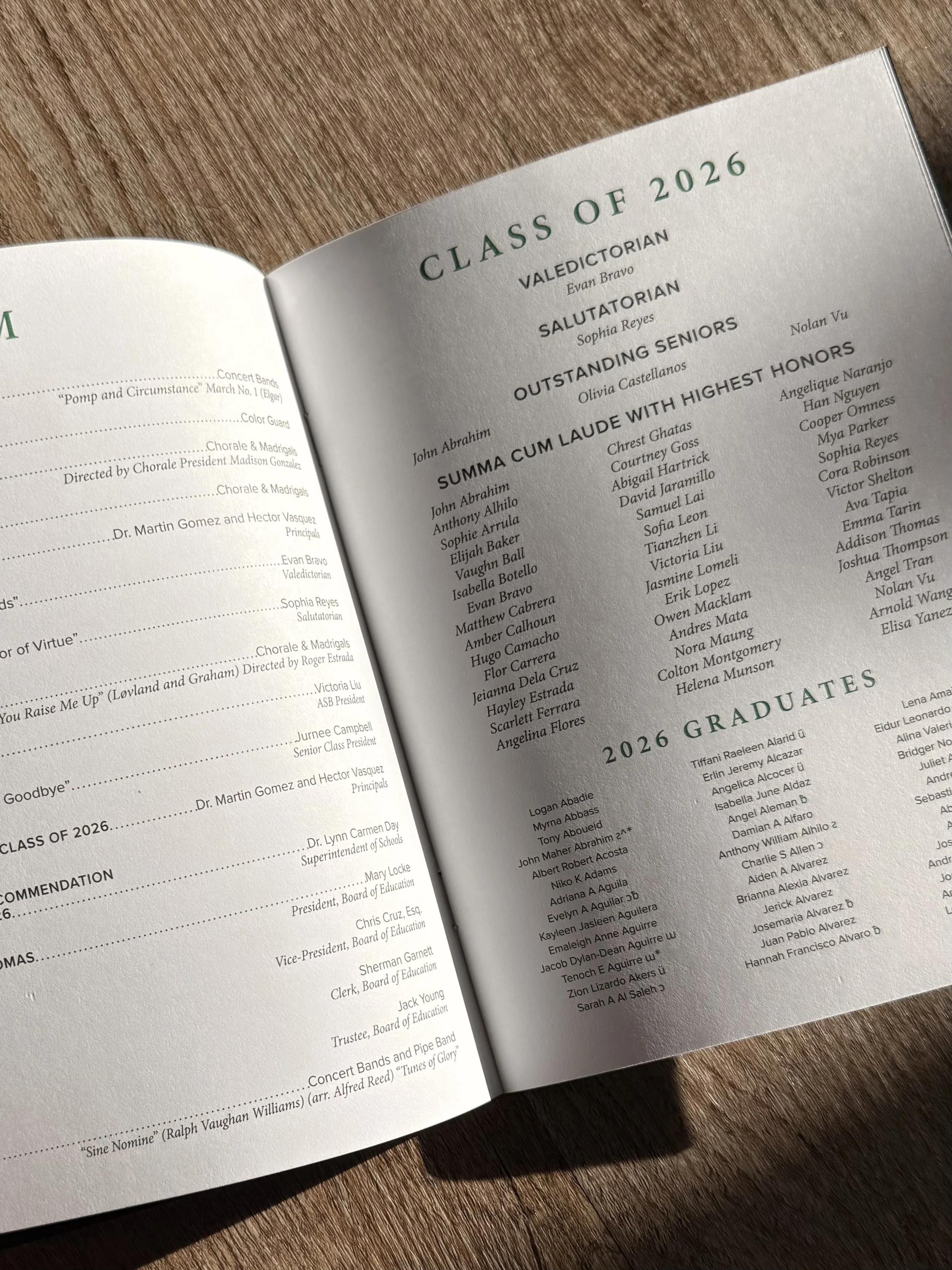 A booklet displaying graduating students' names and honors, titled 'Class of 2026' with categories like 'Valedictorian,' 'Salutatorian,' and 'Outstanding Seniors,' placed on a wooden surface.