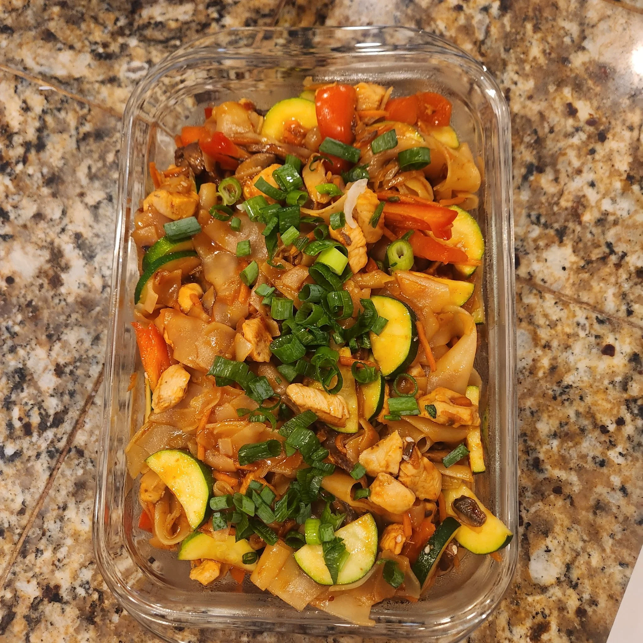 Vegetable stir-fry in a glass container on a granite countertop, topped with chopped green onions.