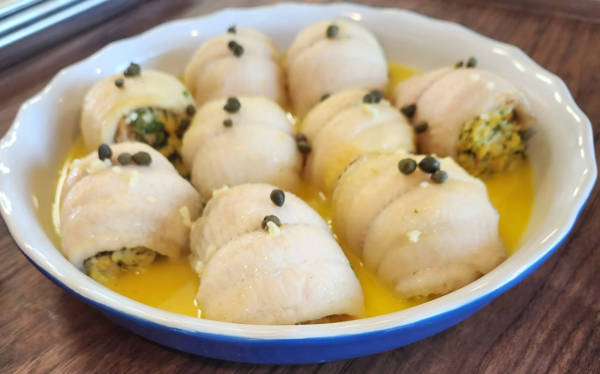 A white ceramic dish filled with stuffed rolled pasta, garnished with black pepper and herbs, in a yellow sauce.