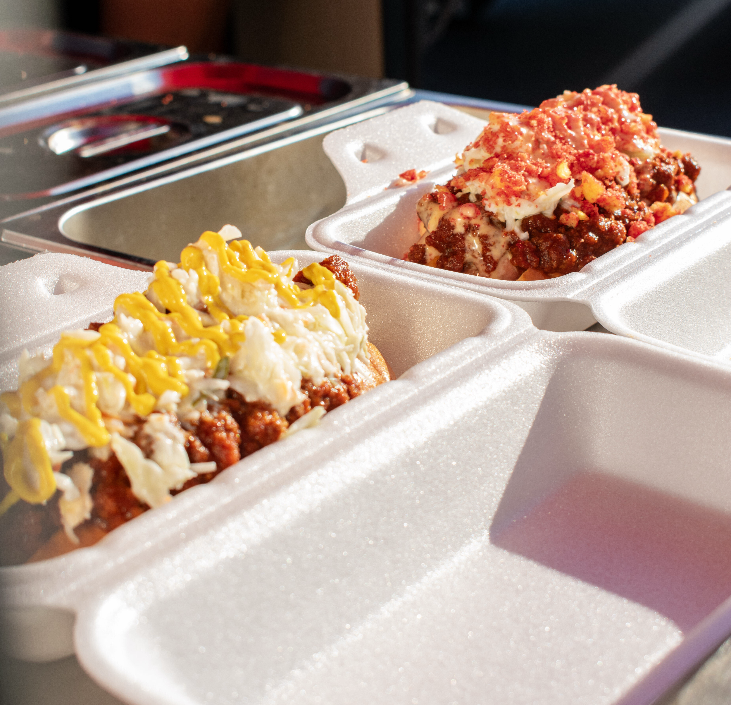 Two foam containers with portions of candy or dessert topped with yellow and red drizzle or syrup.