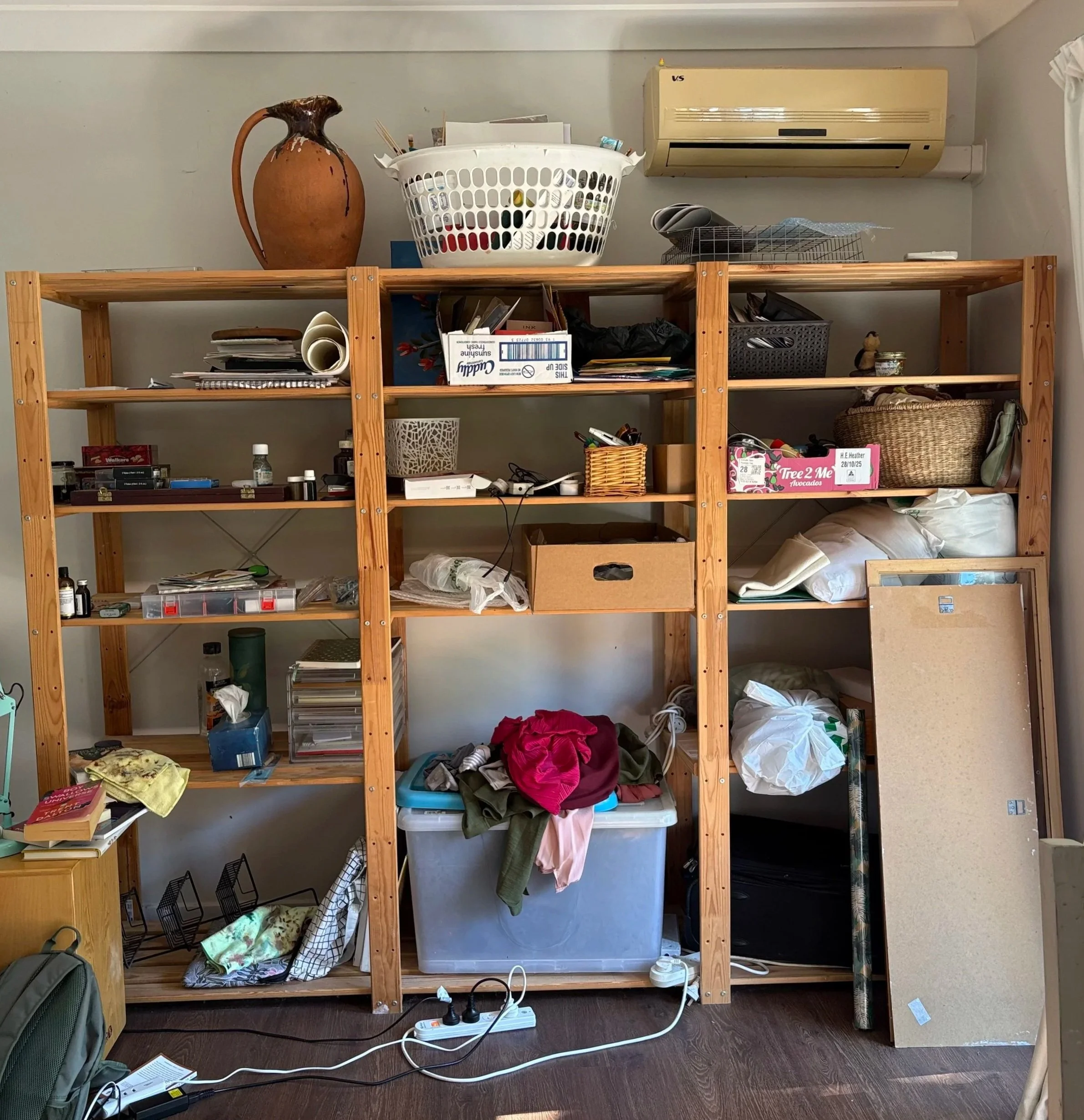 Cluttered multipurpose storage shelves before professional organising, containing art supplies, paperwork, utility items and sentimental belongings. Items are difficult to locate.