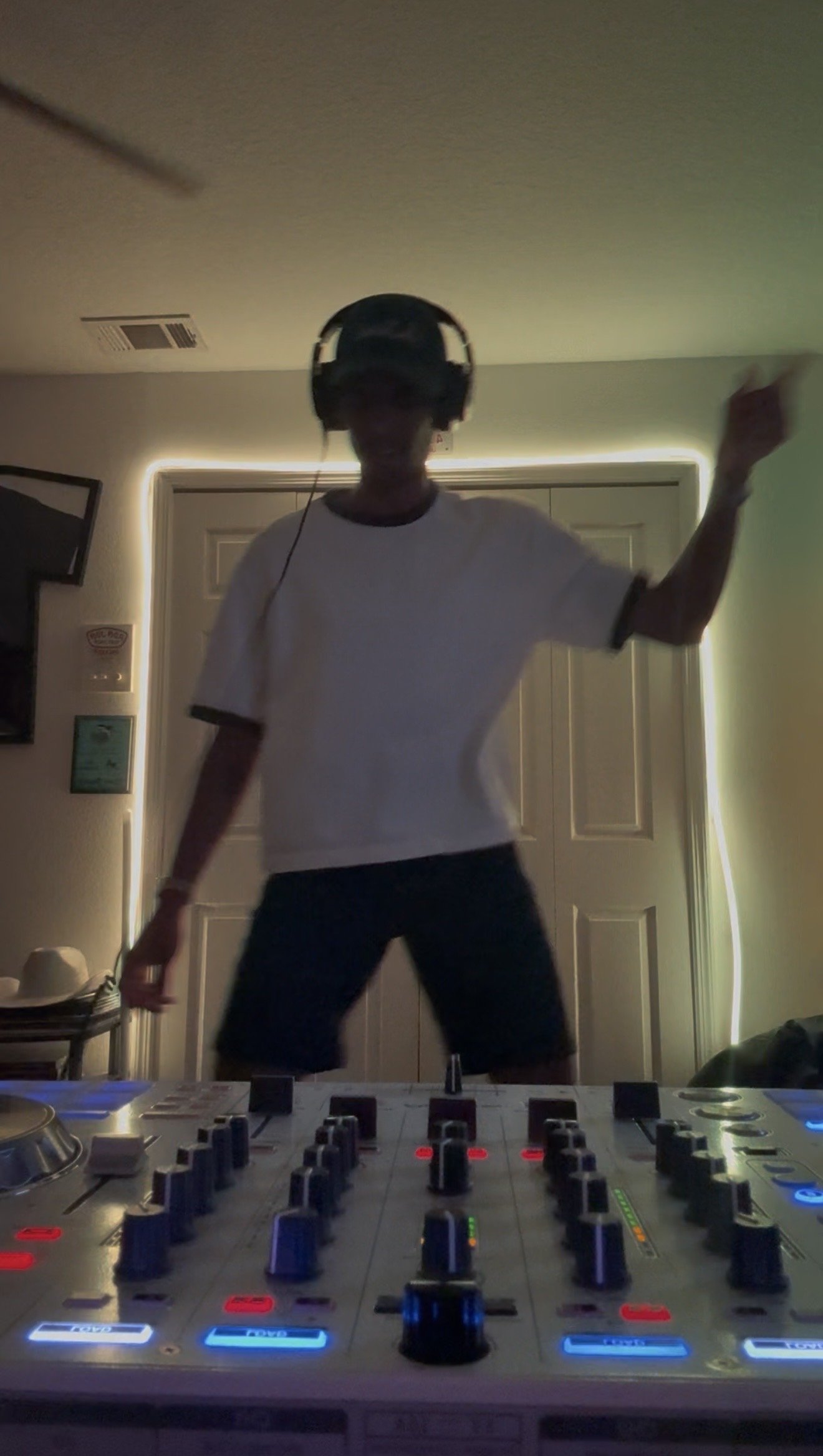 Person dancing in a dimly lit room wearing headphones, with a DJ mixer in the foreground.