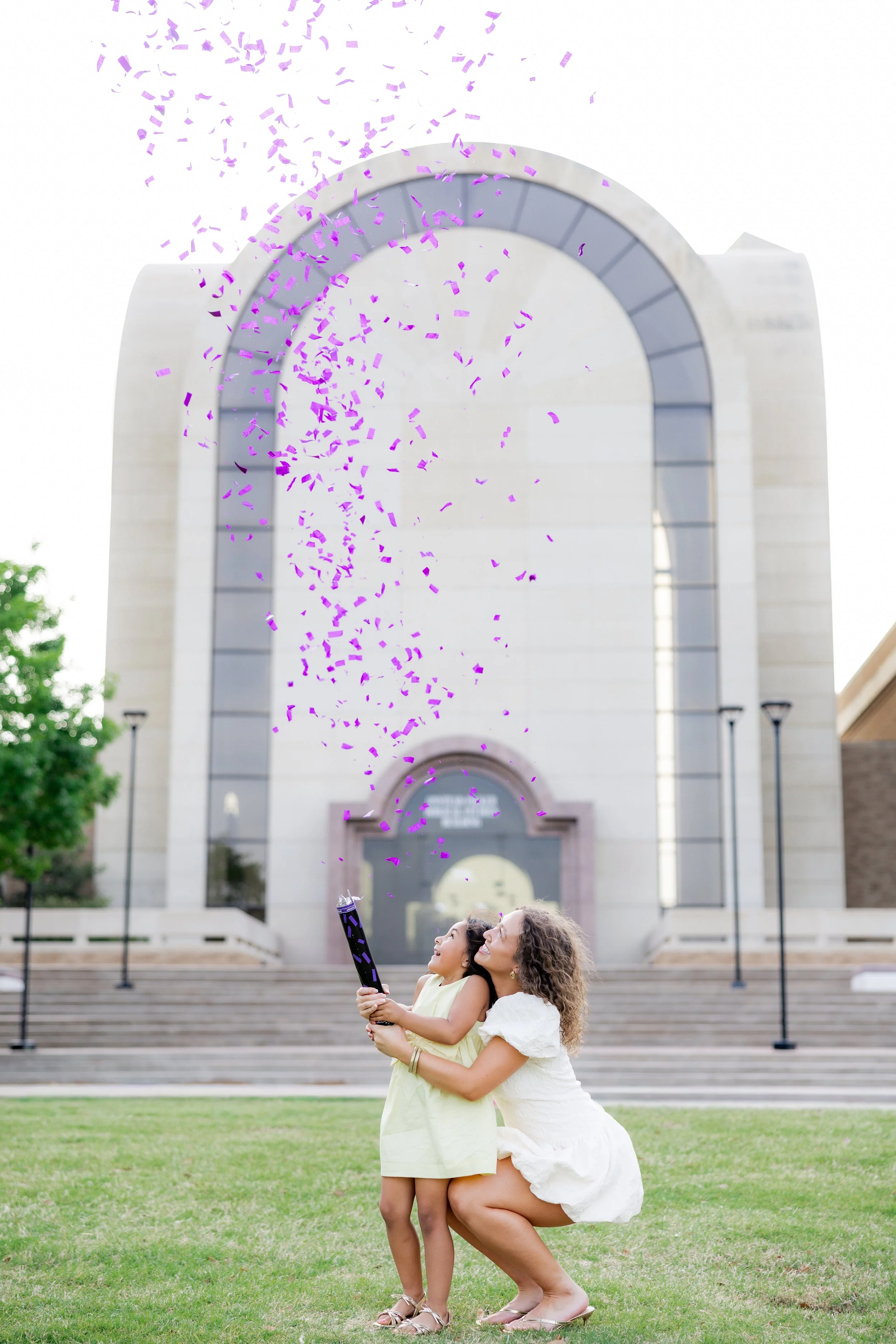 College graduate celebrating with her young daughter and purple confetti during a graduation session.