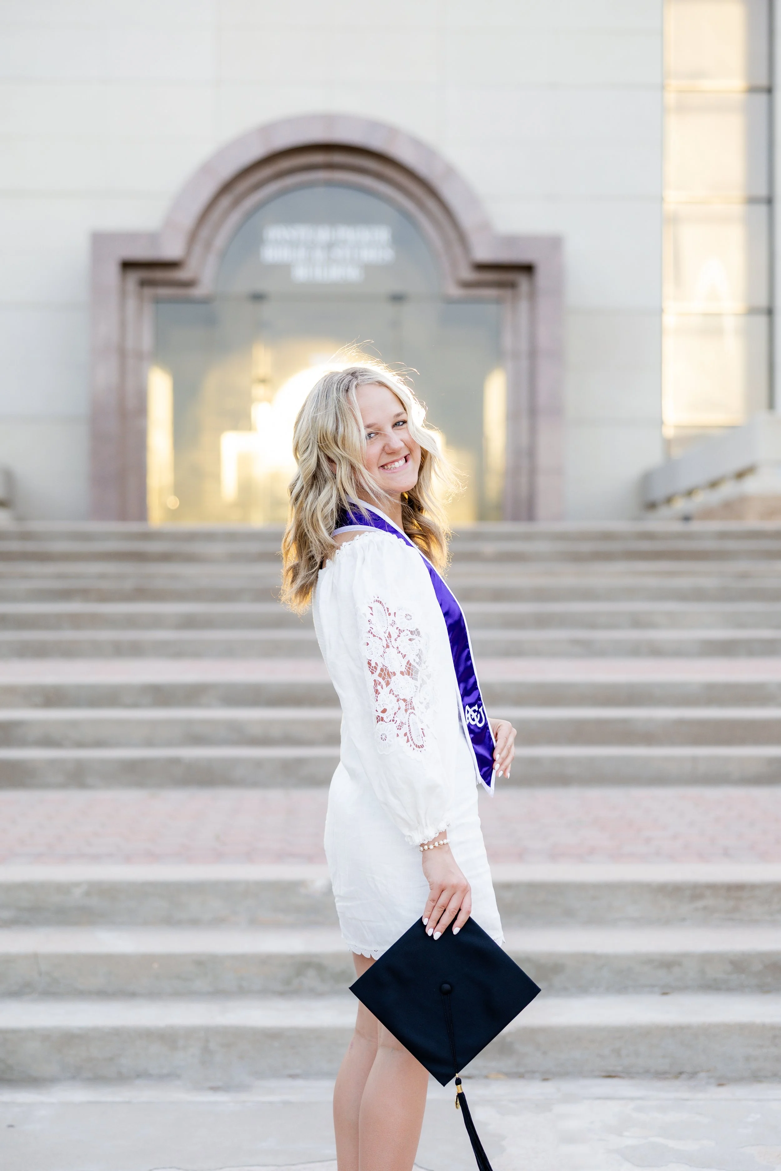 College graduate holding her cap while posing on outdoor steps during a graduation photography session.