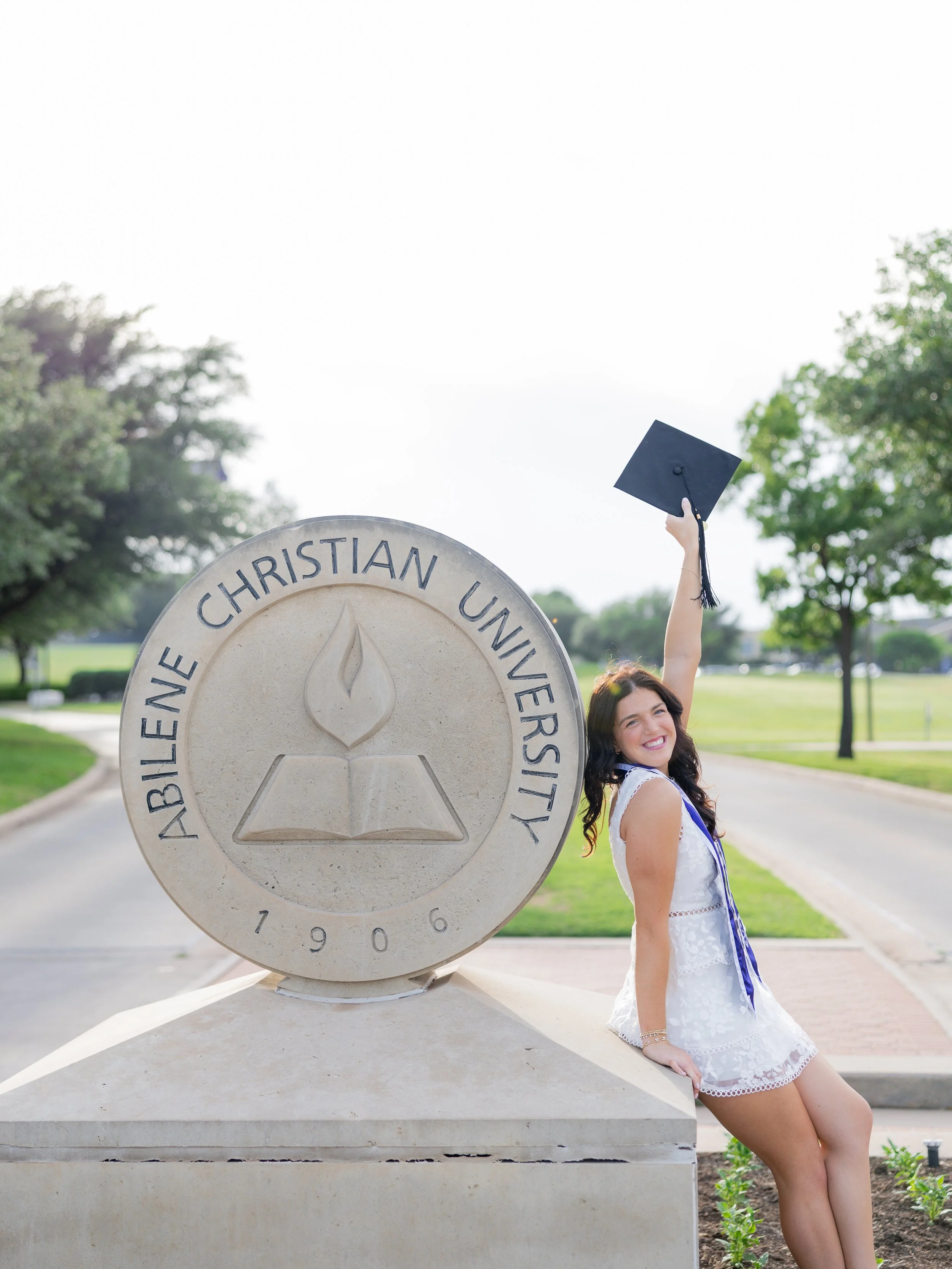 Abilene Christian University graduate celebrating with her graduation cap during an outdoor graduation portrait session.