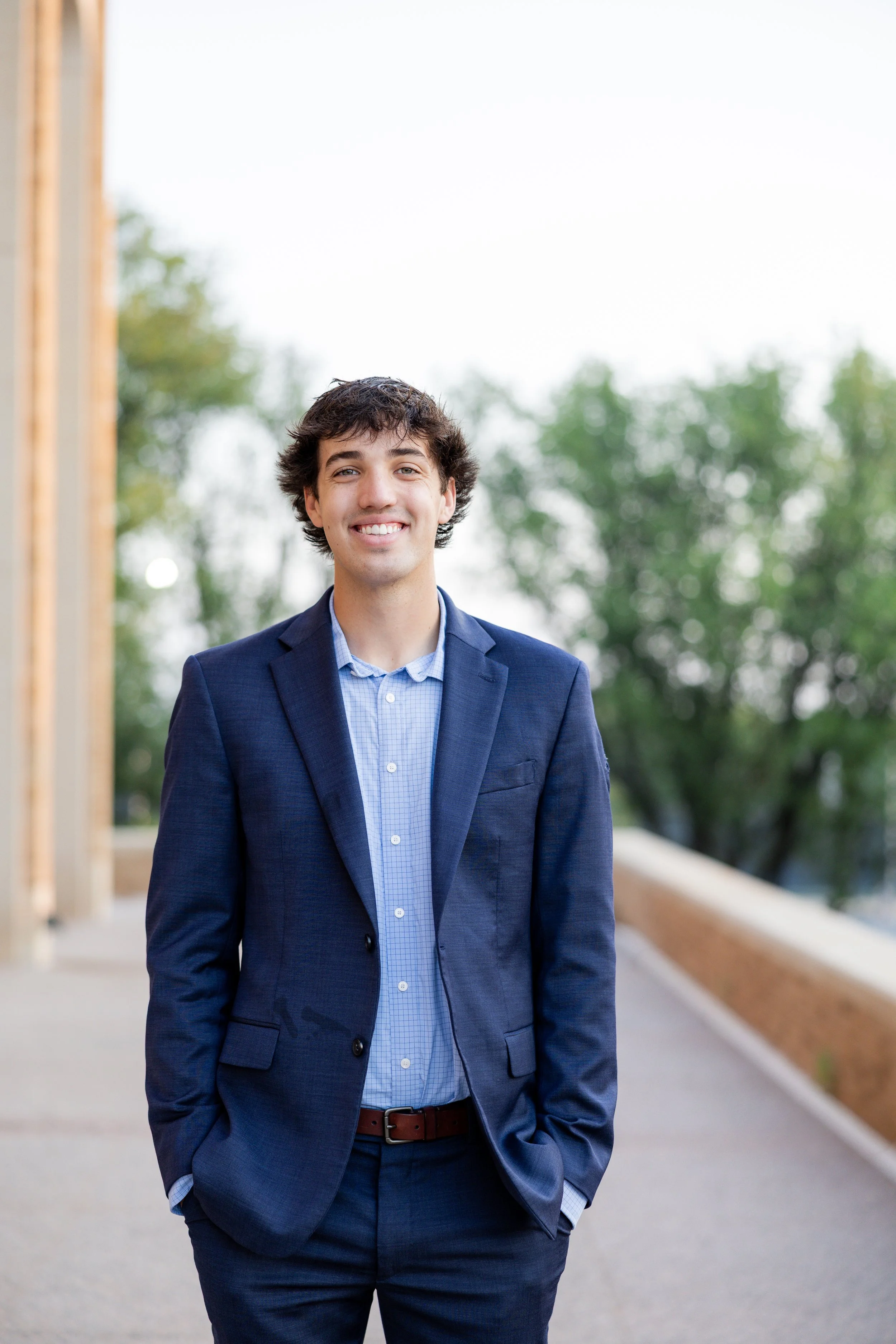 Young man in a blue suit smiling outdoors during a portrait photography session.