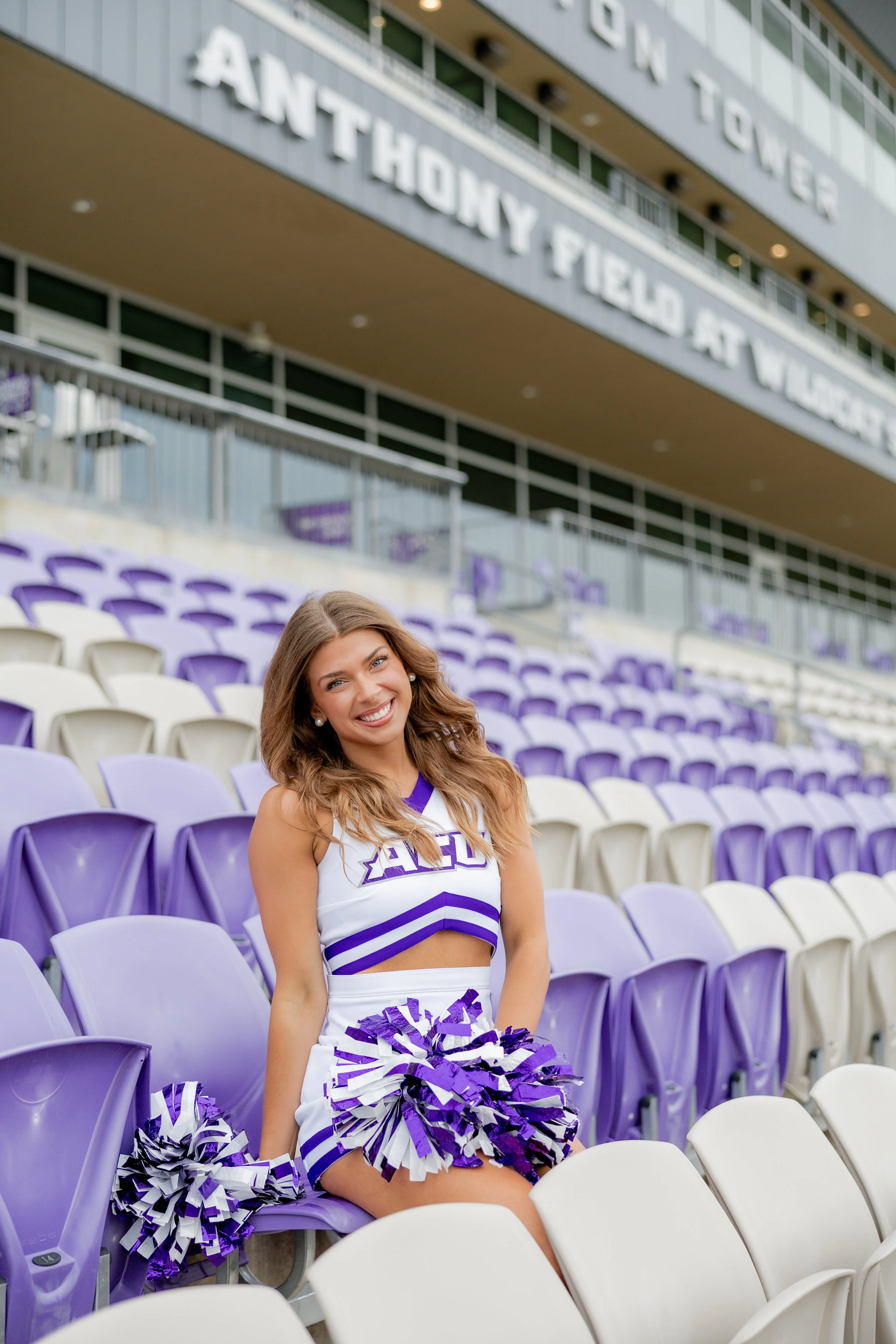 College cheerleader posing with pom-poms in a stadium during a graduation portrait session.