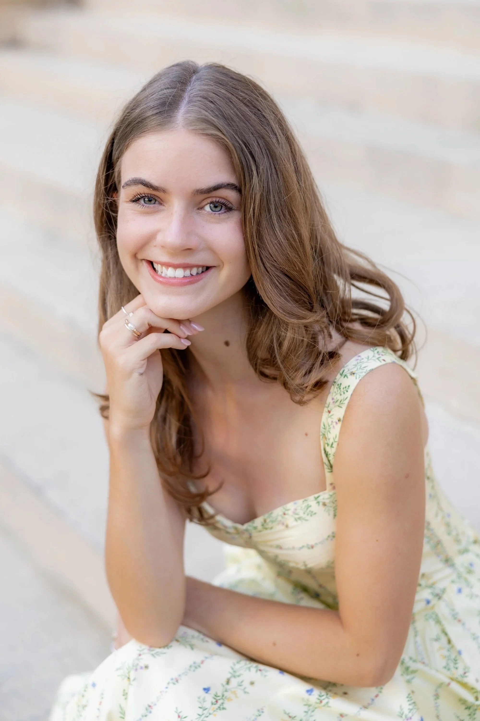 Woman in a yellow floral dress smiling during an outdoor portrait photography session.
