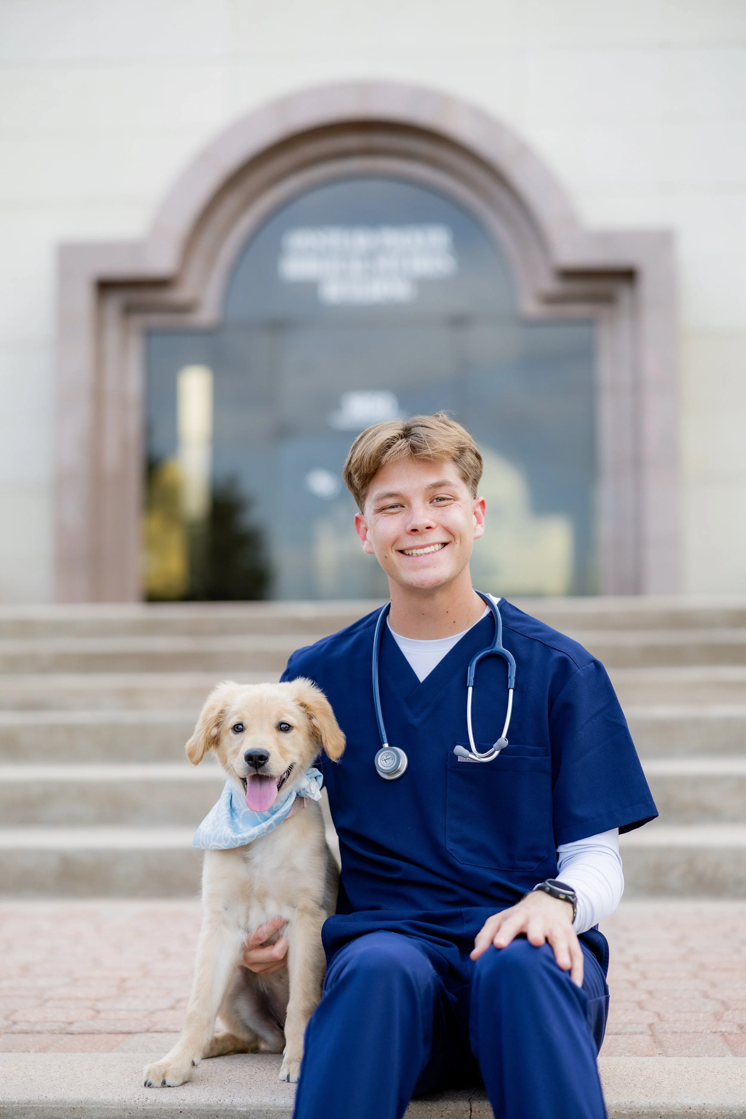 Healthcare graduate in scrubs posing with a golden retriever puppy during a college graduation session.