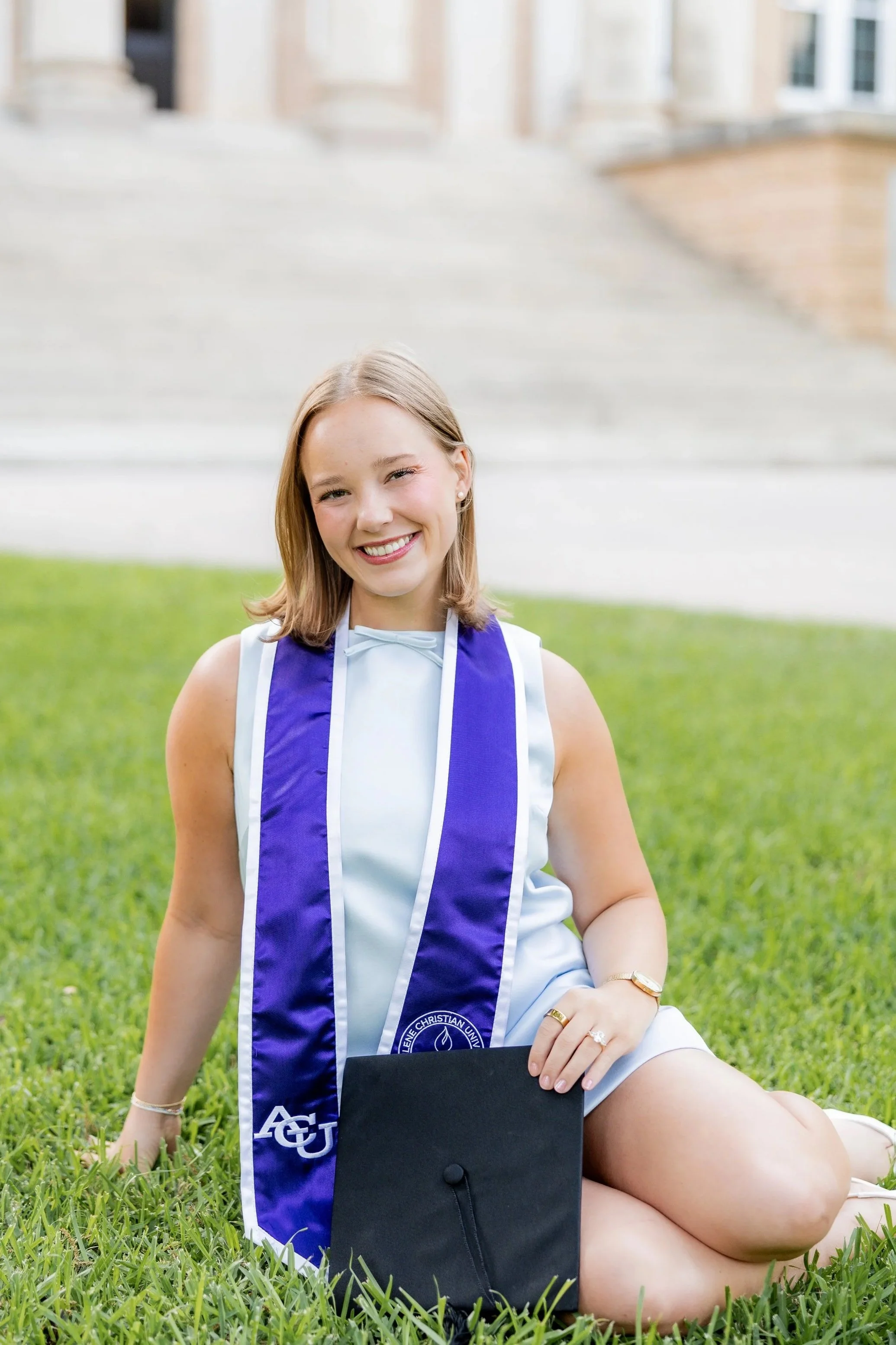 College graduate in a graduation stole posing with her cap and diploma during an outdoor graduation session.