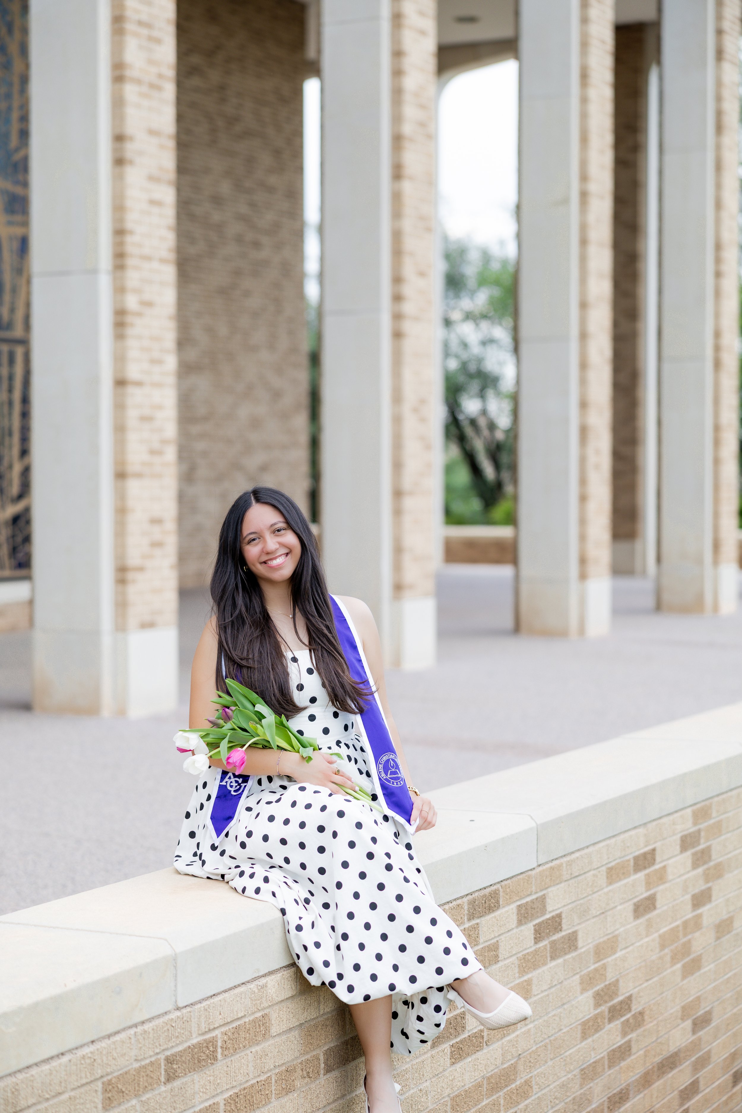 College graduate in a graduation stole holding a bouquet of tulips during an outdoor graduation session.
