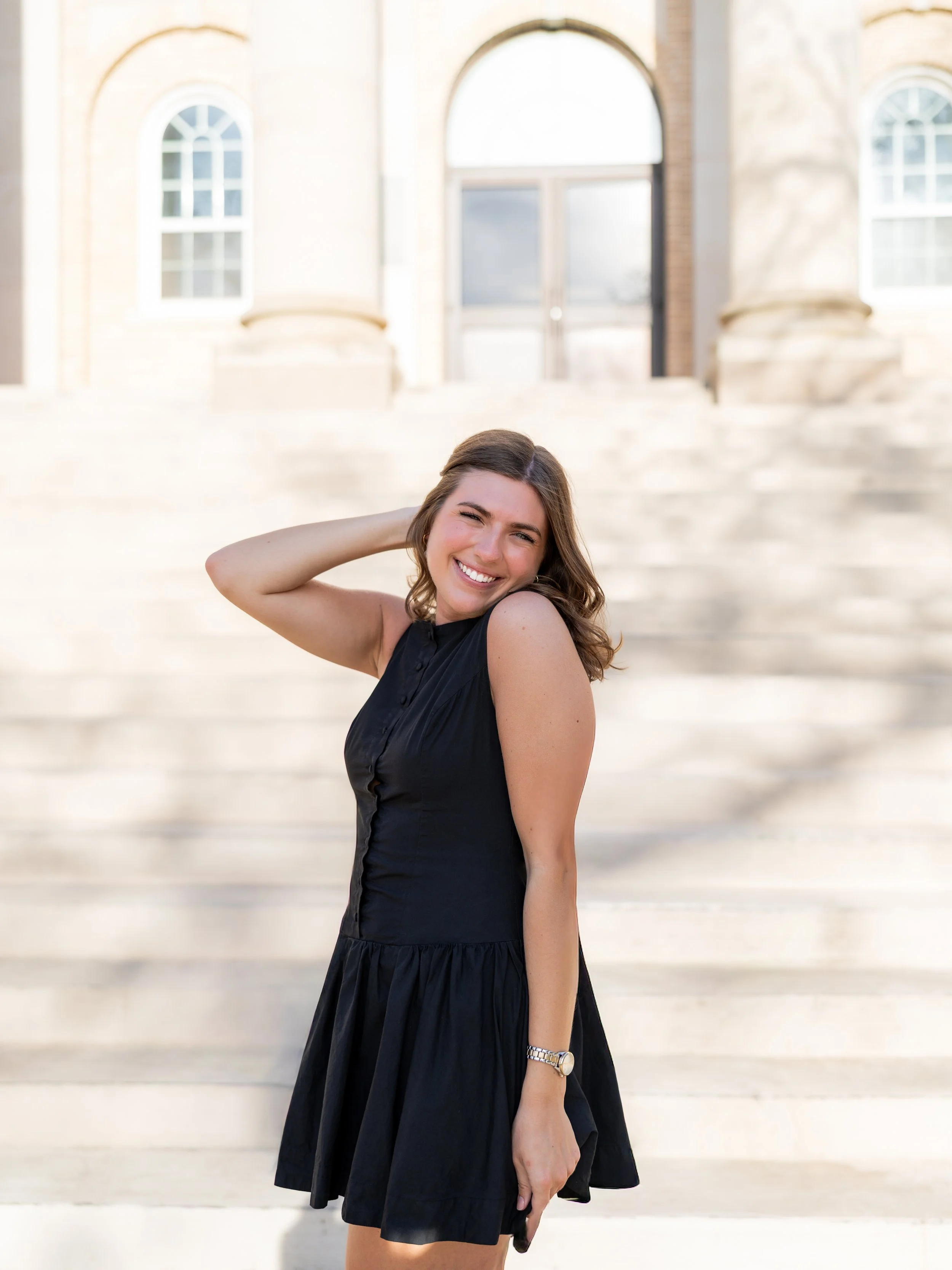 Woman in a black dress posing on outdoor steps during a portrait photography session.