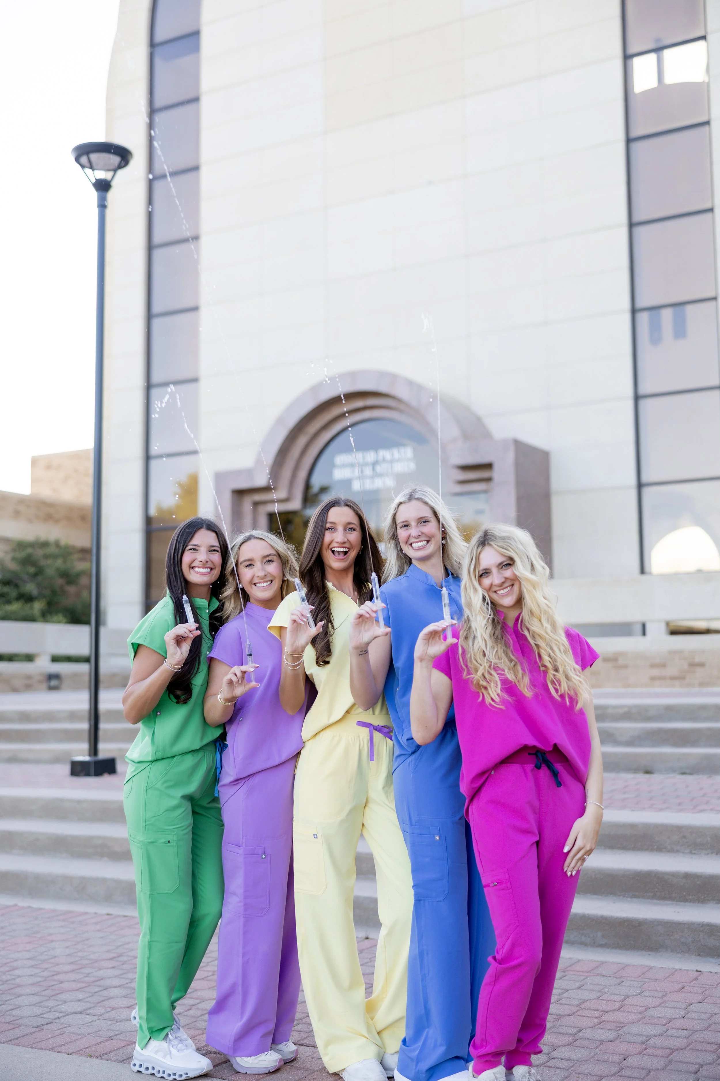 Group of nursing graduates in colorful scrubs celebrating together during a college graduation session.