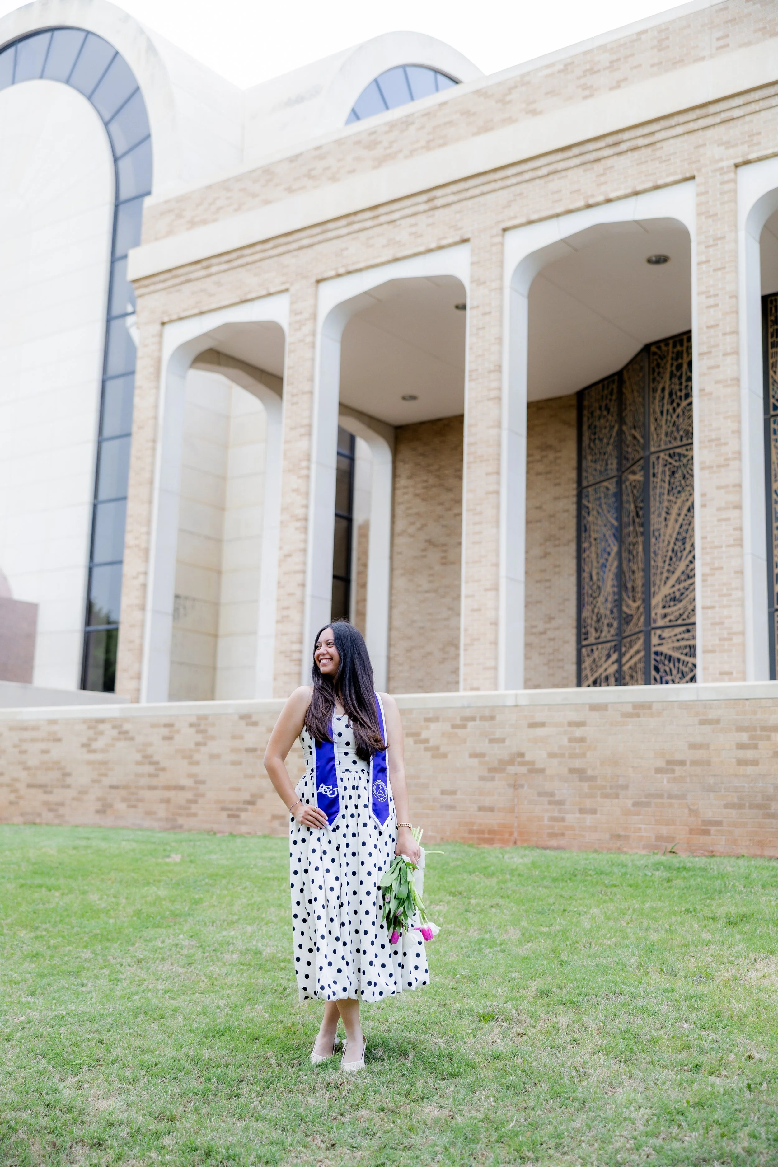 College graduate holding a bouquet of flowers while posing outdoors in her graduation stole.