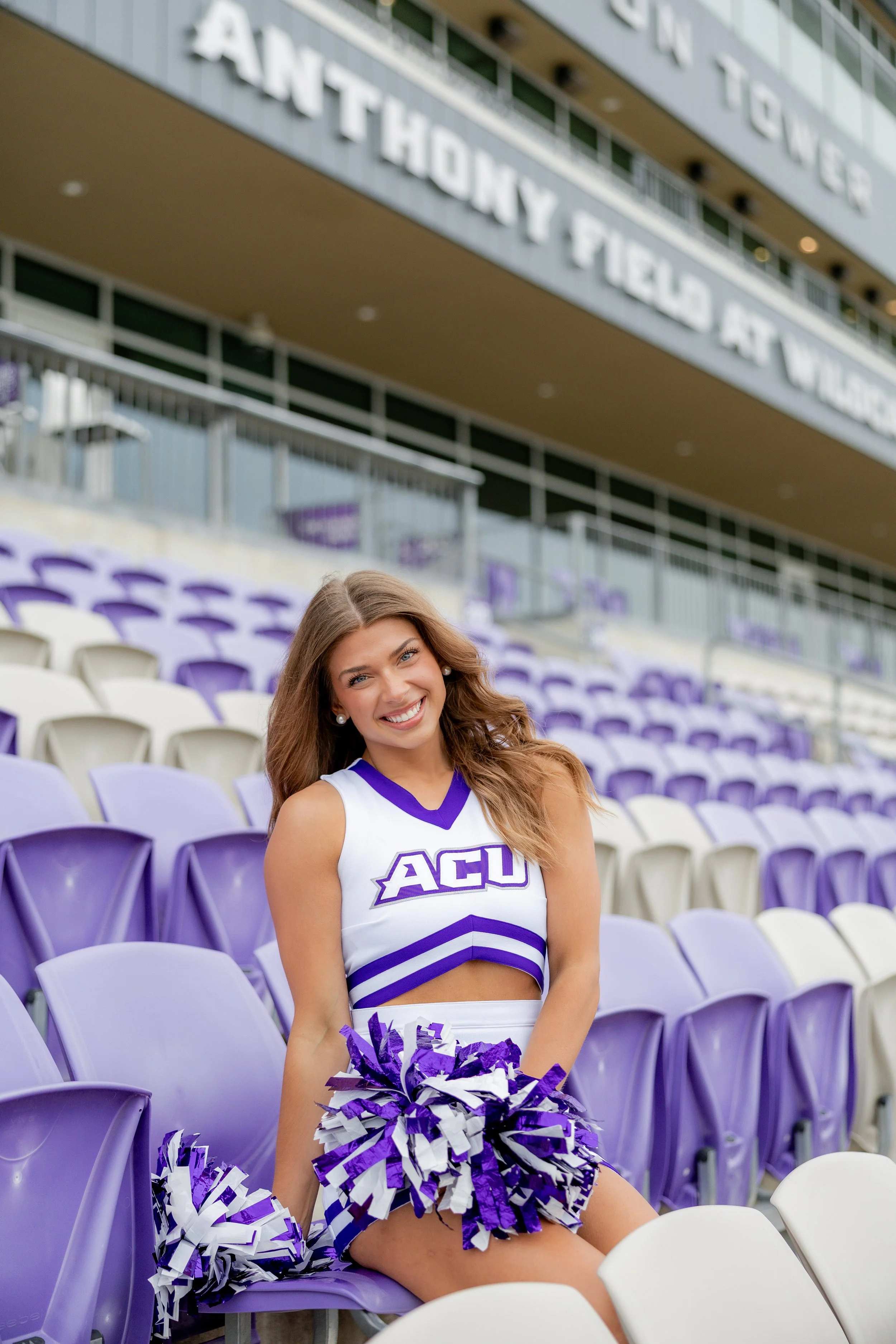 College cheerleader posing with pom-poms in a stadium during a graduation portrait session.