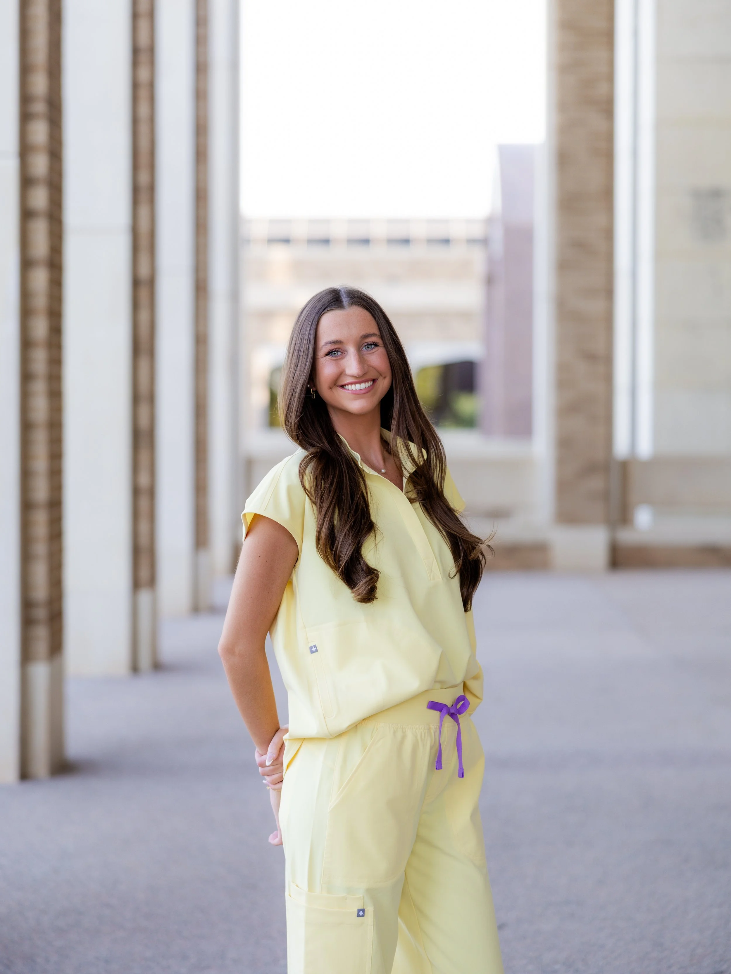Nursing graduate in yellow scrubs posing outdoors during a college graduation photography session.