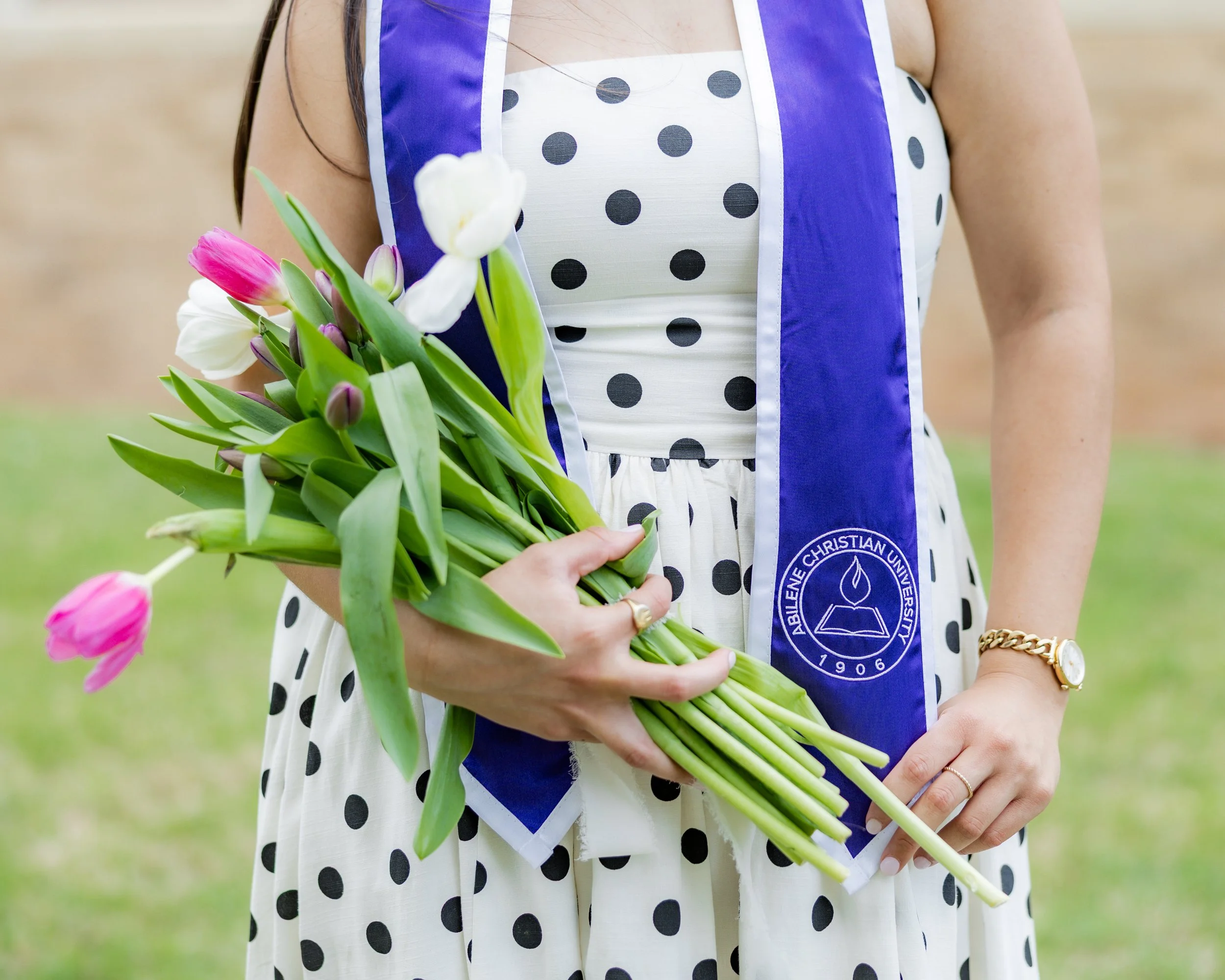 College graduate in cap and gown holding a bouquet of pink and white tulips.
