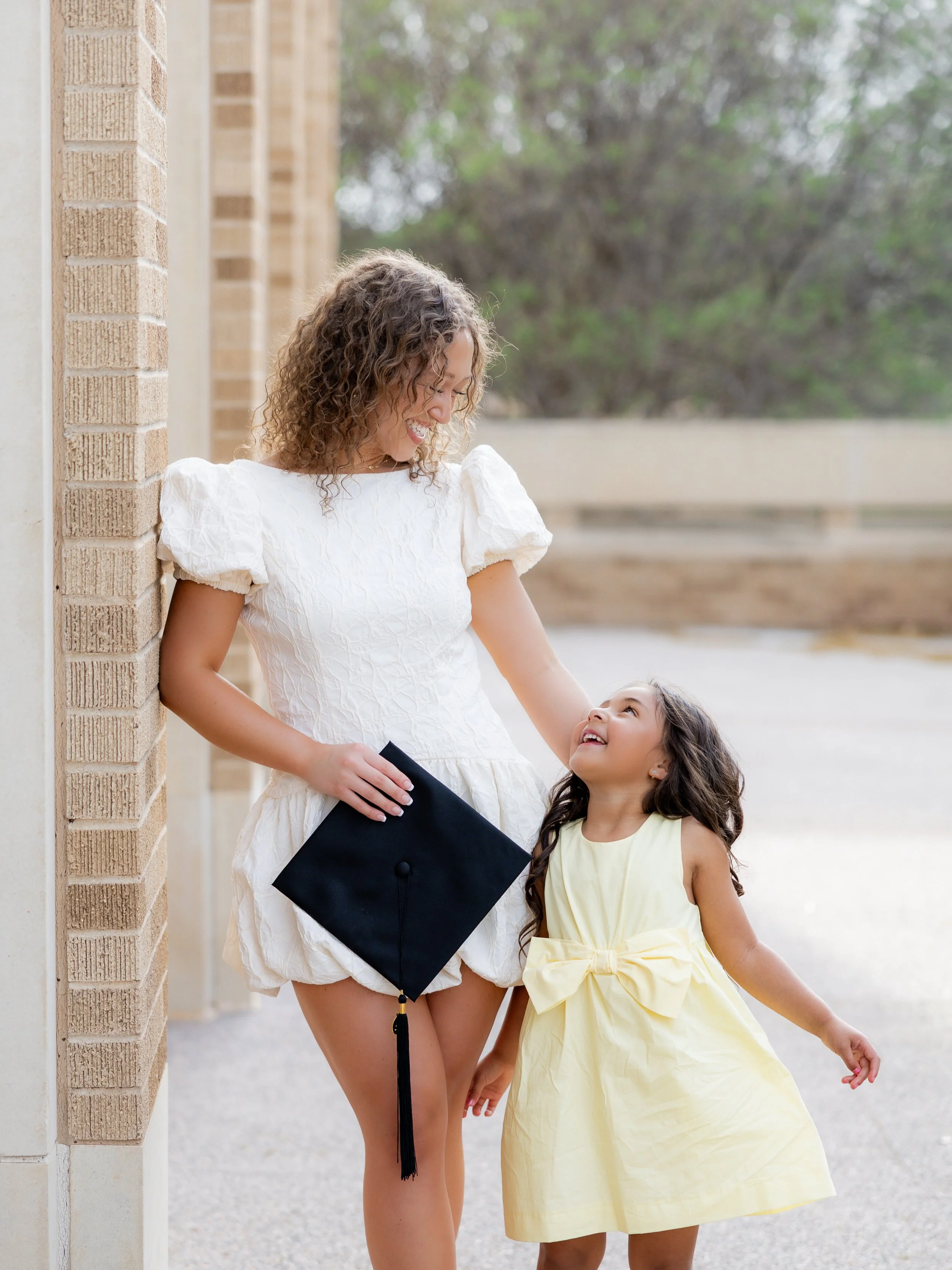 College graduate sharing a sweet moment with her young daughter during an outdoor graduation session.