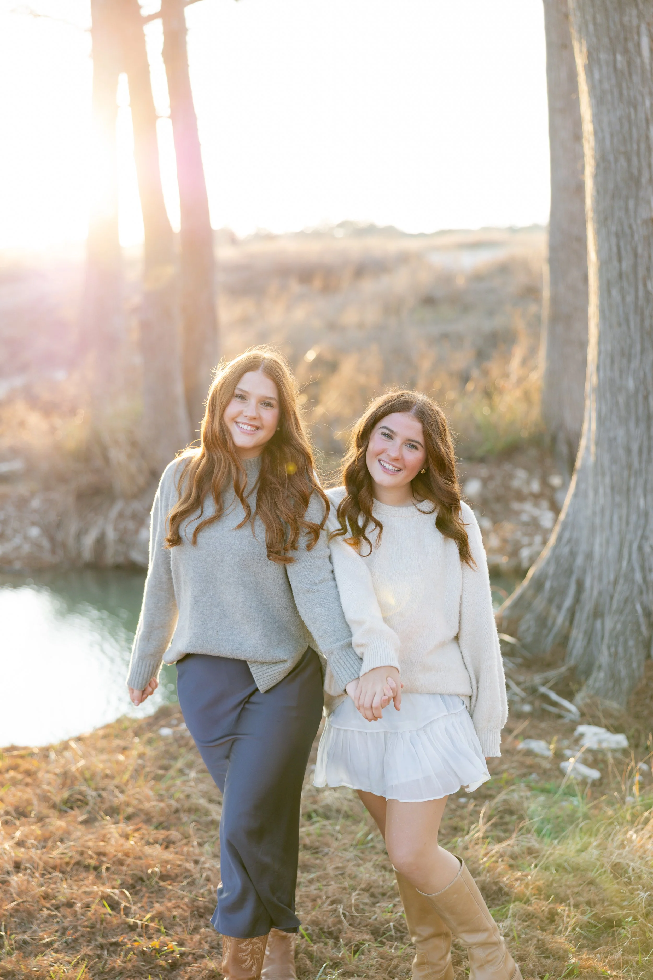Two sisters holding hands and walking together during an outdoor family portrait session at golden hour.