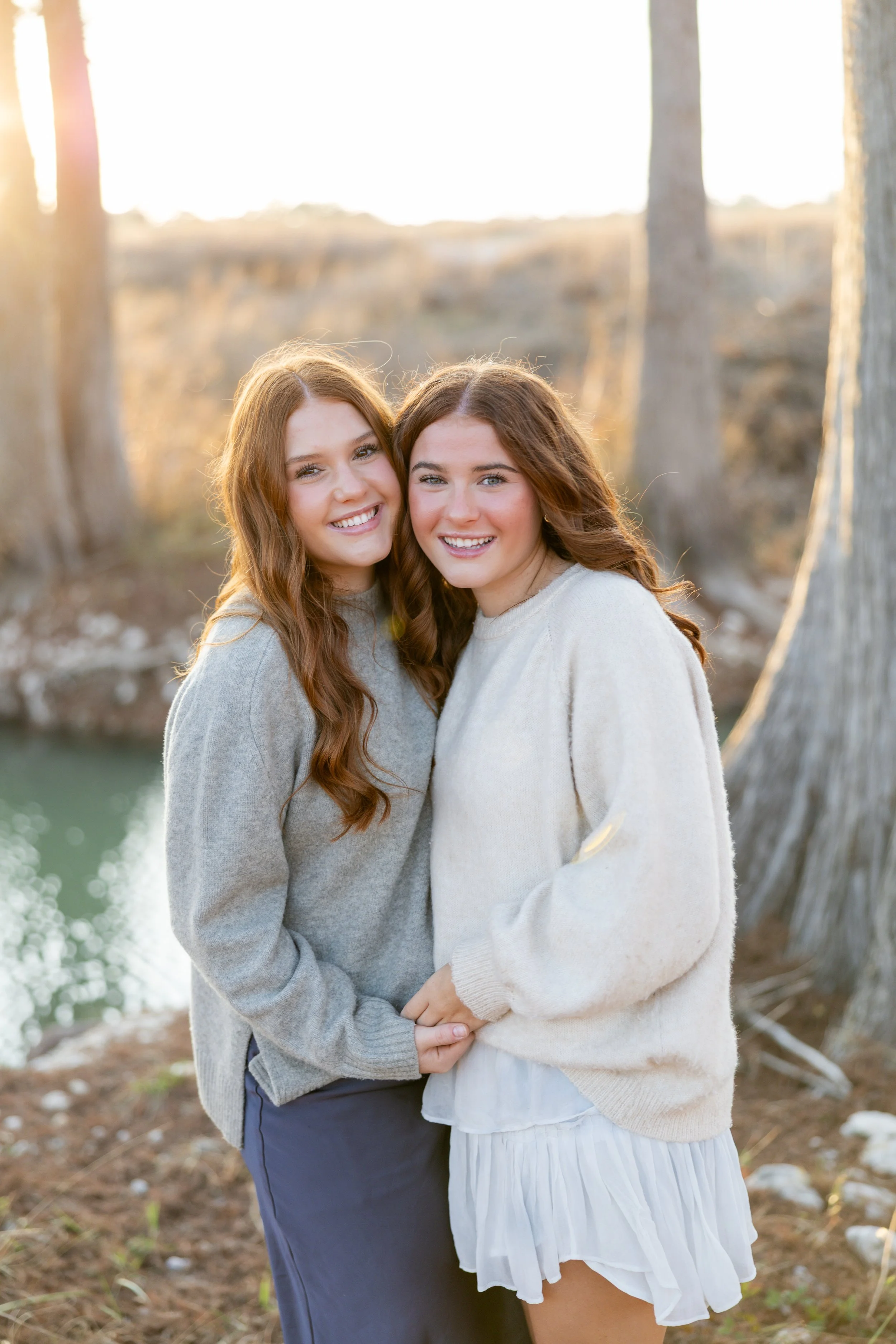 Two sisters smiling together during an outdoor family portrait session at sunset.