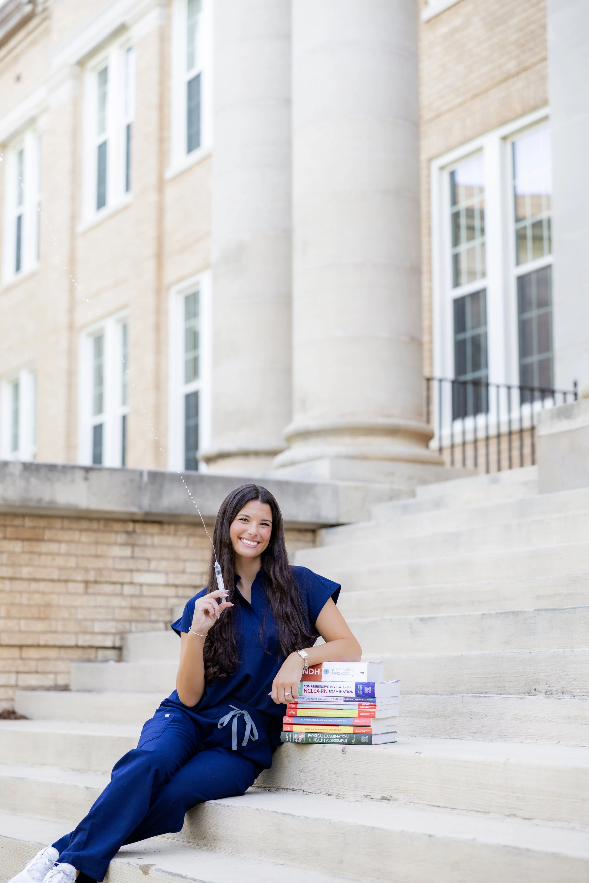Nursing graduate in scrubs posing with medical textbooks during a college graduation session.