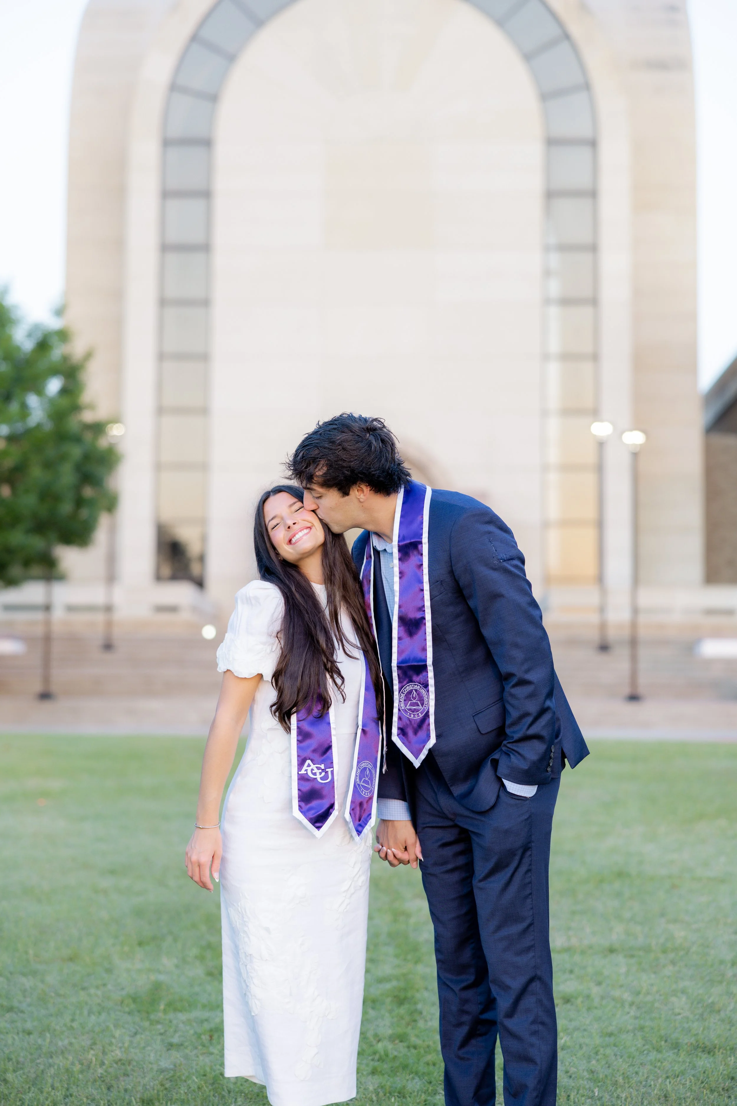 Graduate couple holding hands and celebrating together during an outdoor graduation couple photography session.